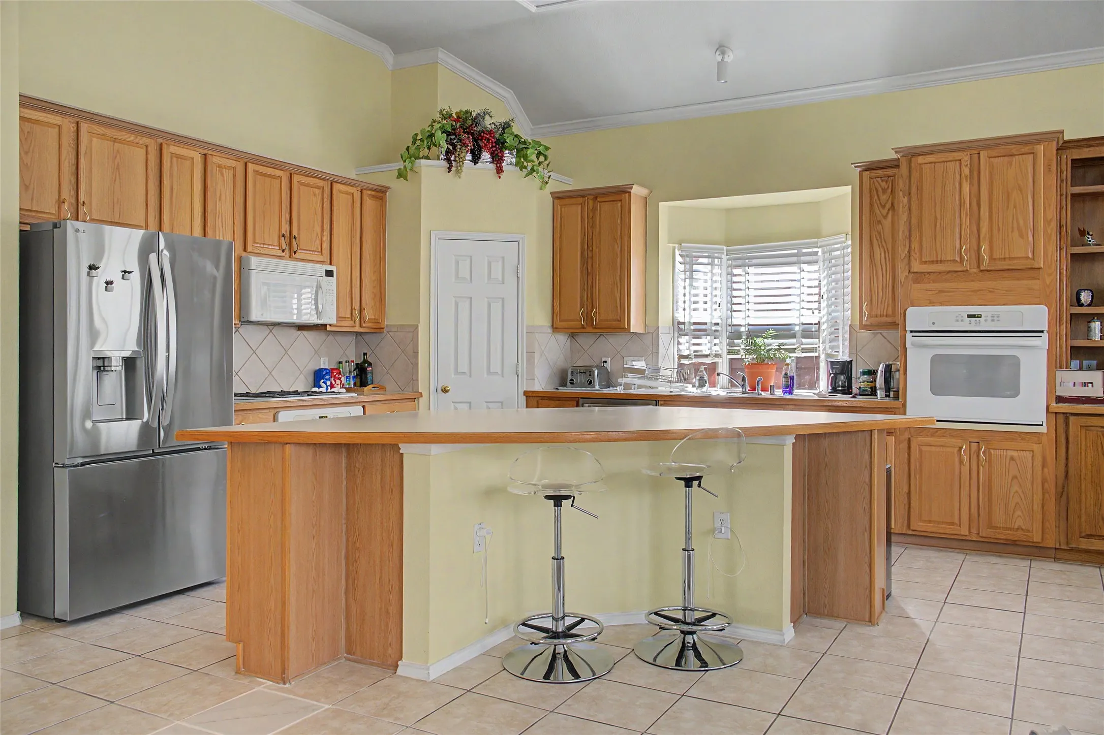 Light wood-finish cabinetry, built-in oven, tile flooring, and bay window