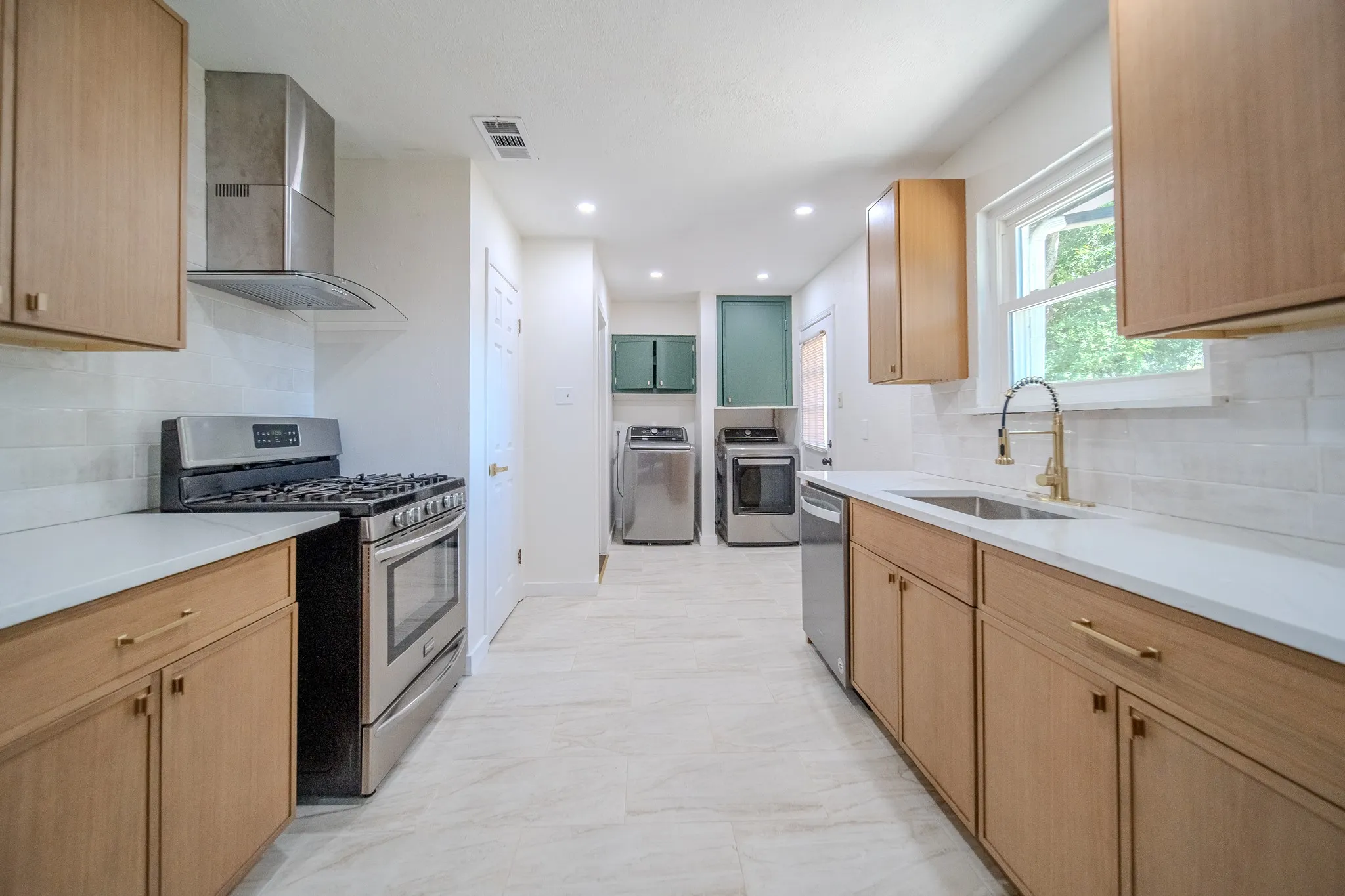 Kitchen featuring light wood-finish cabinetry, white countertops, stainless steel appliances, and a white subway tile backsplash