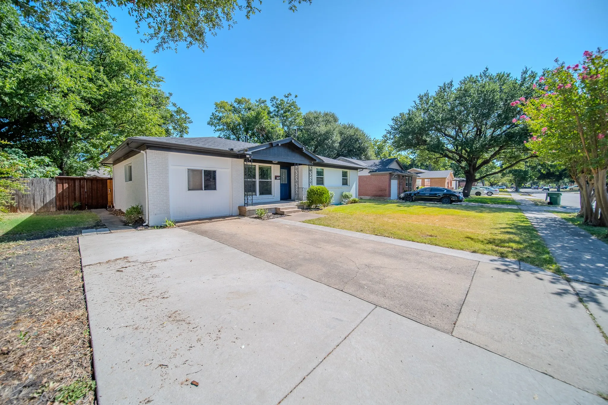White painted brick exterior with a contrasting dark roof, a concrete driveway, and a partially fenced yard