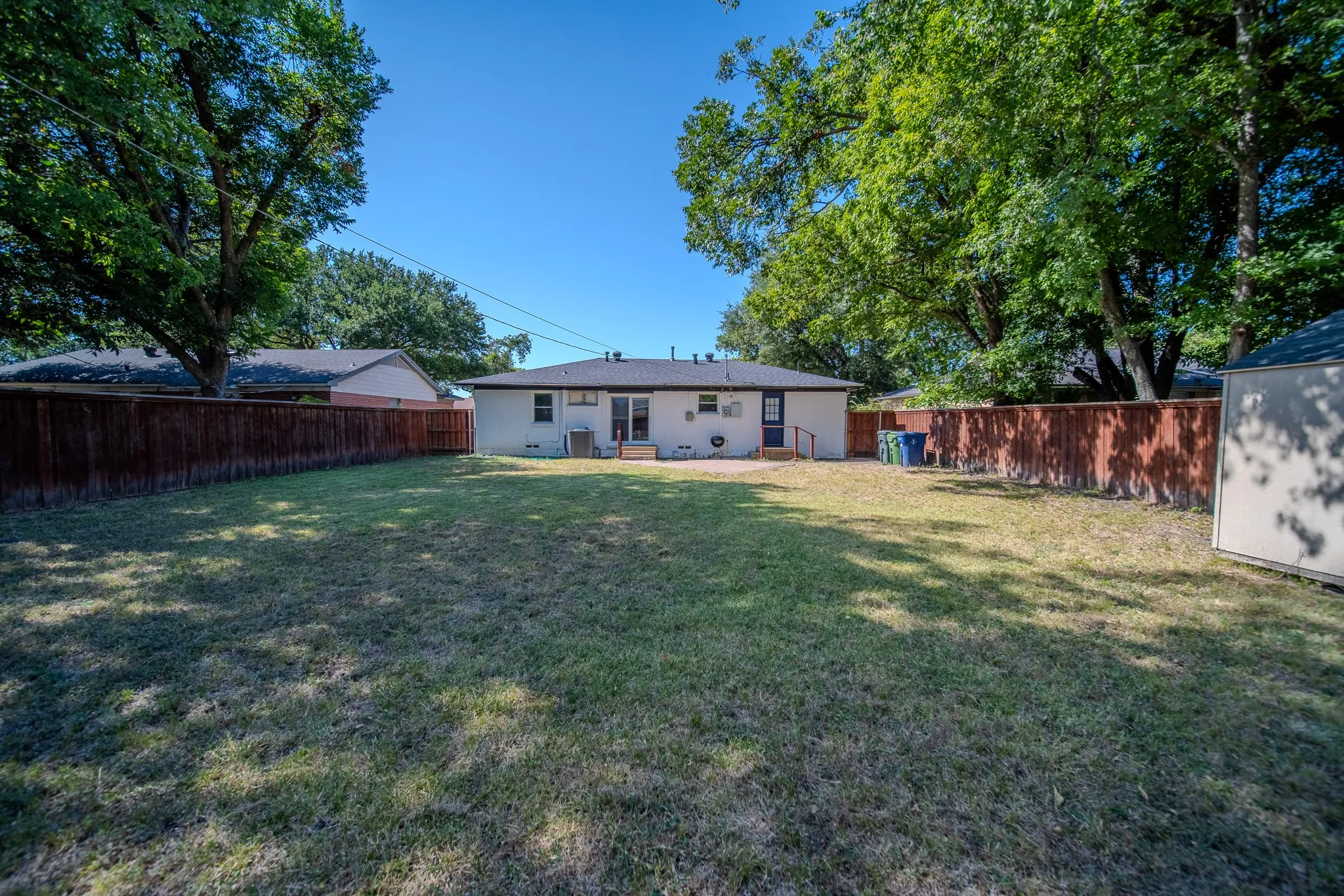 Expansive backyard with a manicured lawn, wood fencing, and mature trees