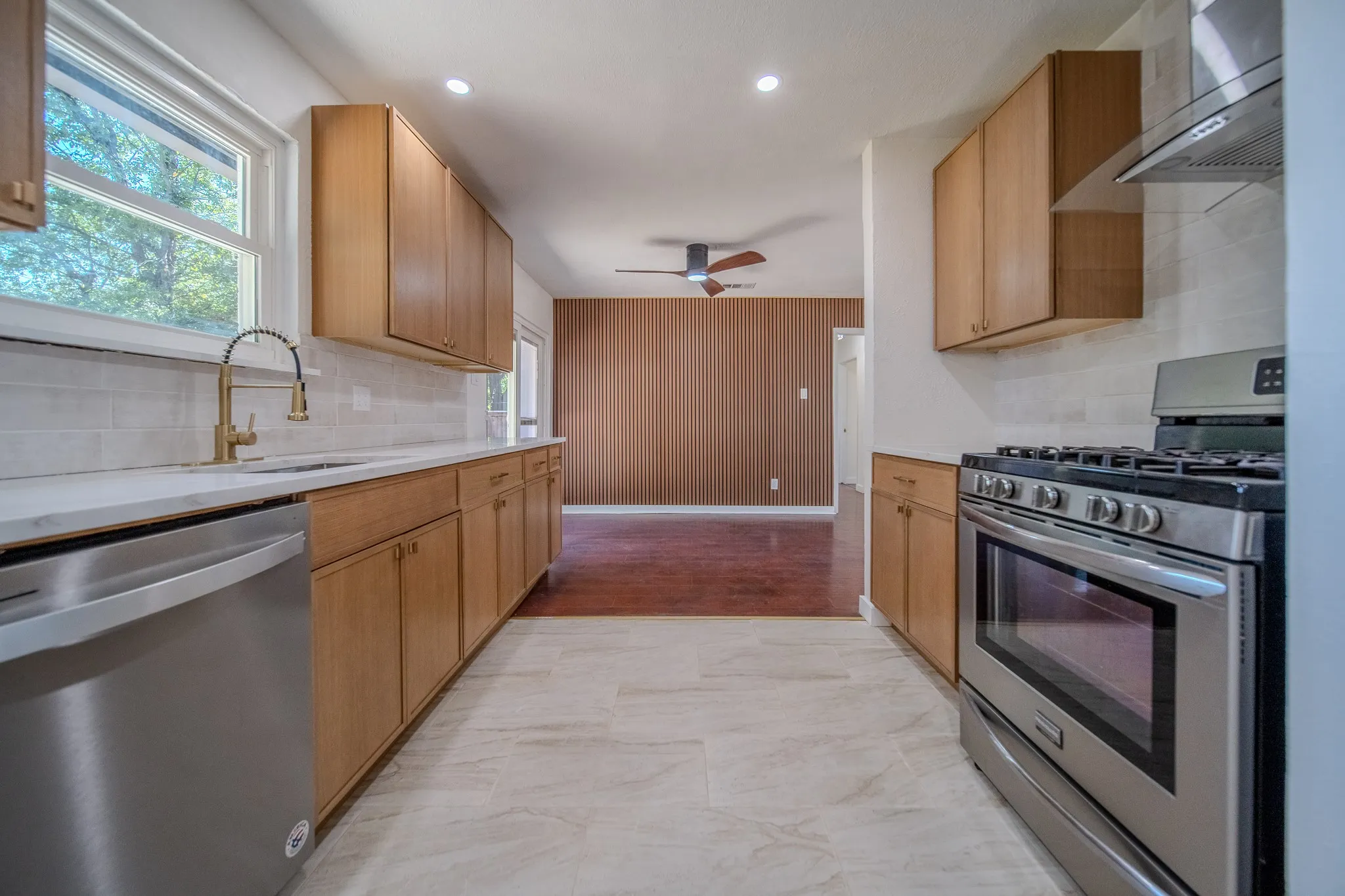Modern kitchen featuring light wood cabinetry, stainless steel appliances, a white tile backsplash, and a gold-tone pull-down faucet