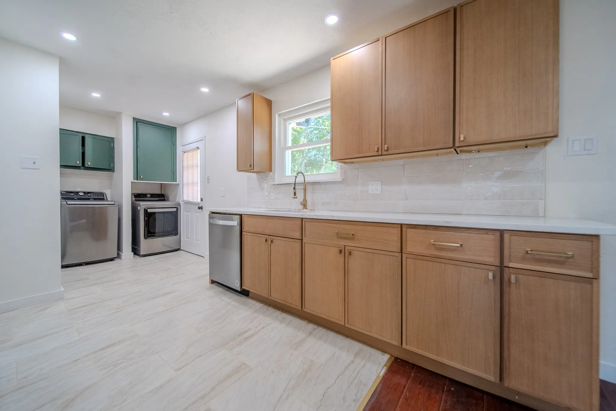 Recessed lighting illuminates wood-finish cabinetry, a light-toned countertop, and a tiled backsplash
