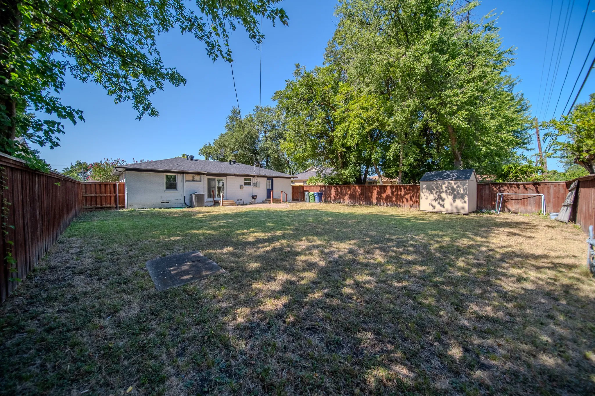 Expansive backyard with a wooden fence, mature trees, and a detached storage shed