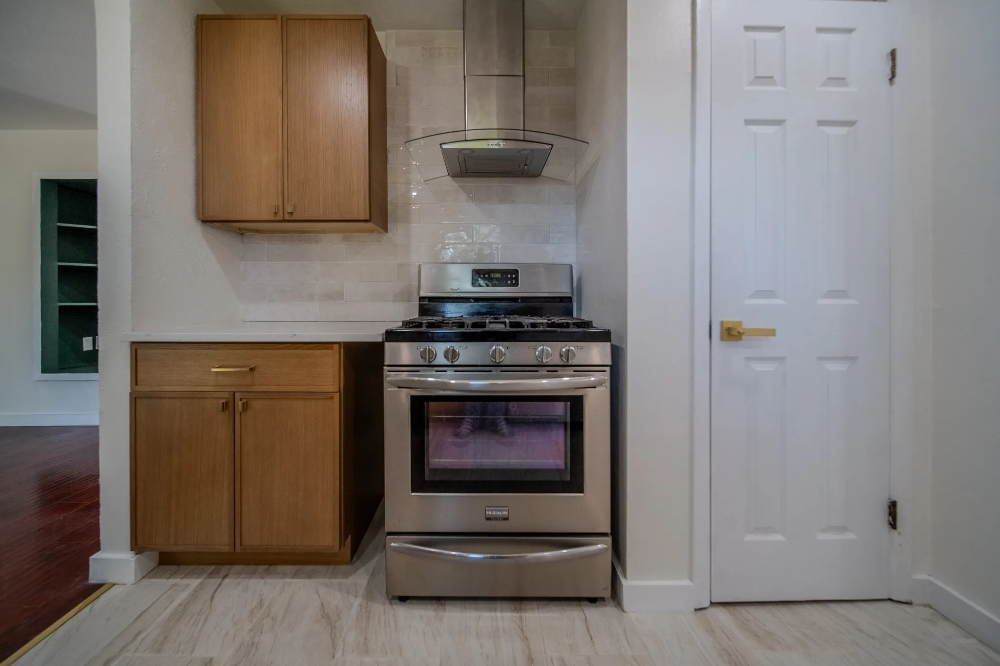Stainless steel range and hood, light wood-finish cabinetry, tile backsplash, solid surface countertop, and wood-finish flooring