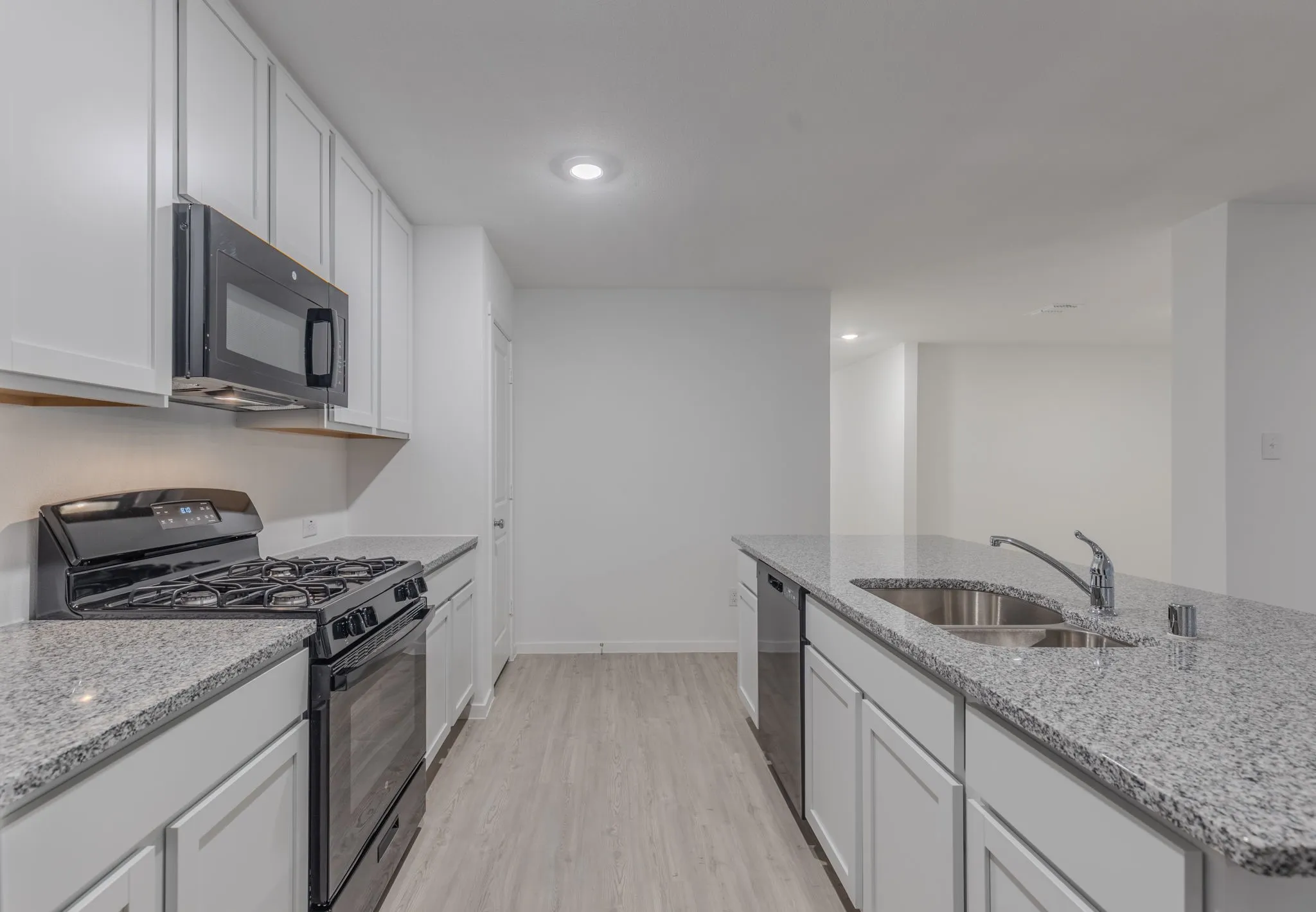 Kitchen with black appliances, light stone counters, white cabinets, and sink