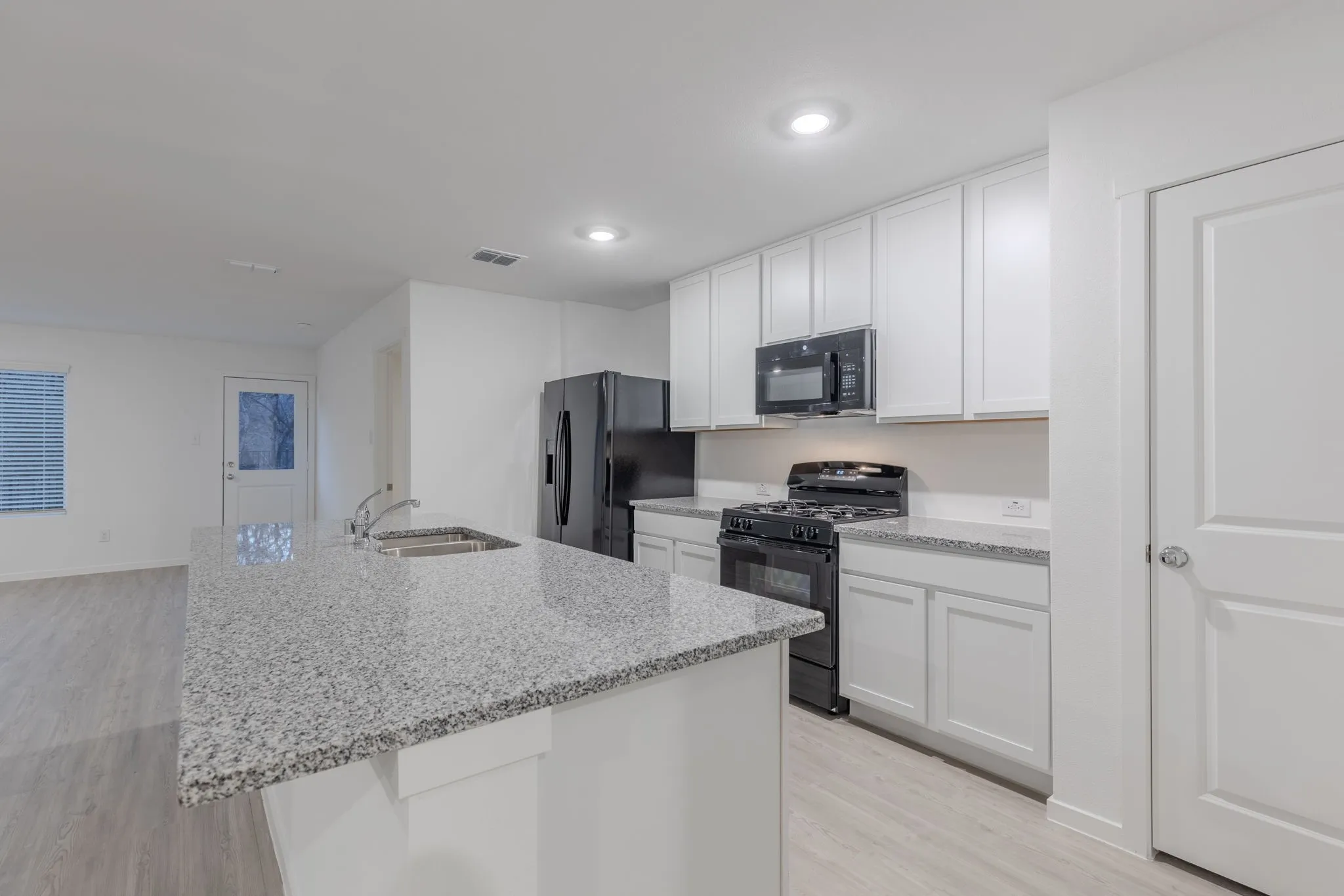 Kitchen with black appliances, a center island with sink, sink, light wood-type flooring, and white cabinetry