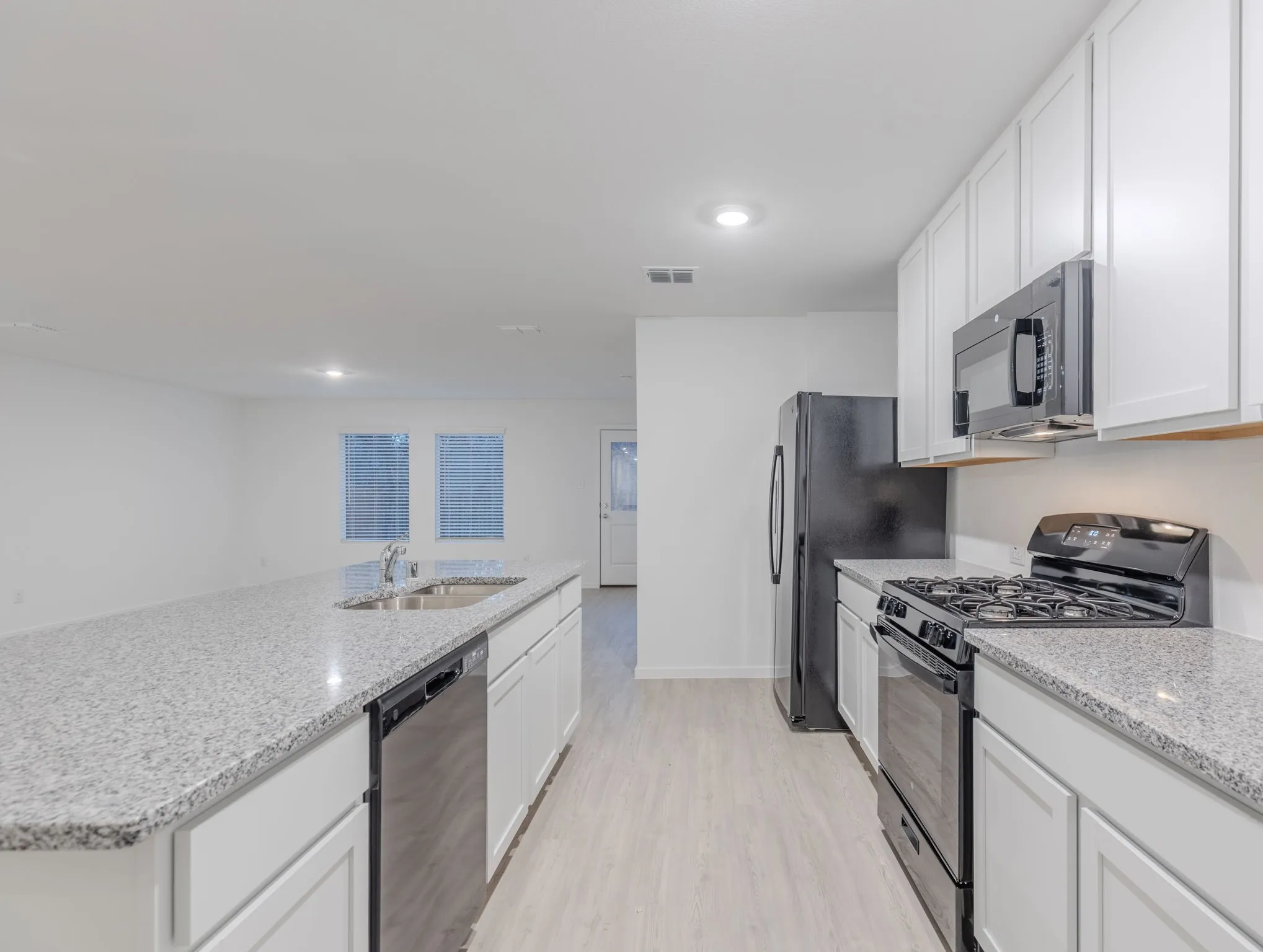 Kitchen featuring black appliances, sink, light stone countertops, light wood-type flooring, and white cabinetry