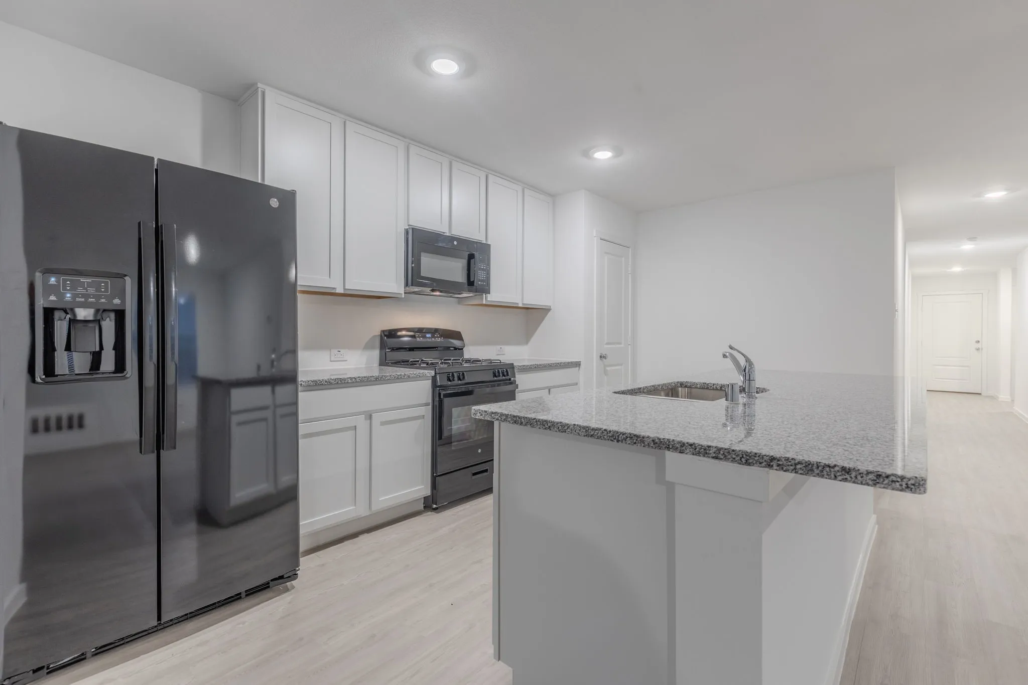 Kitchen featuring white cabinetry, sink, an island with sink, black appliances, and light wood-type flooring