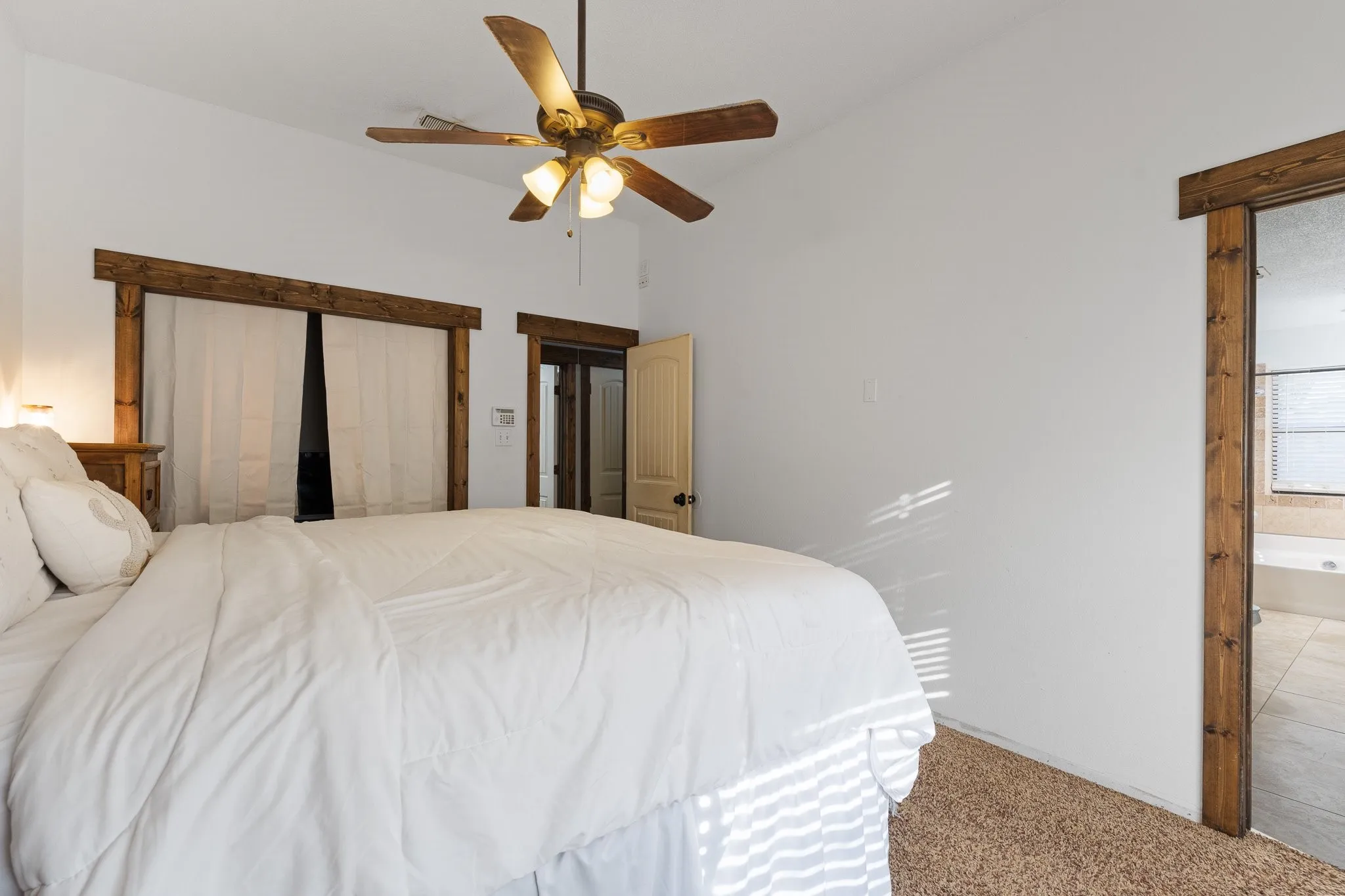 Carpet flooring, ceiling fan with integrated lighting, wood-finish door frames, and a built-in bathtub in the adjacent room