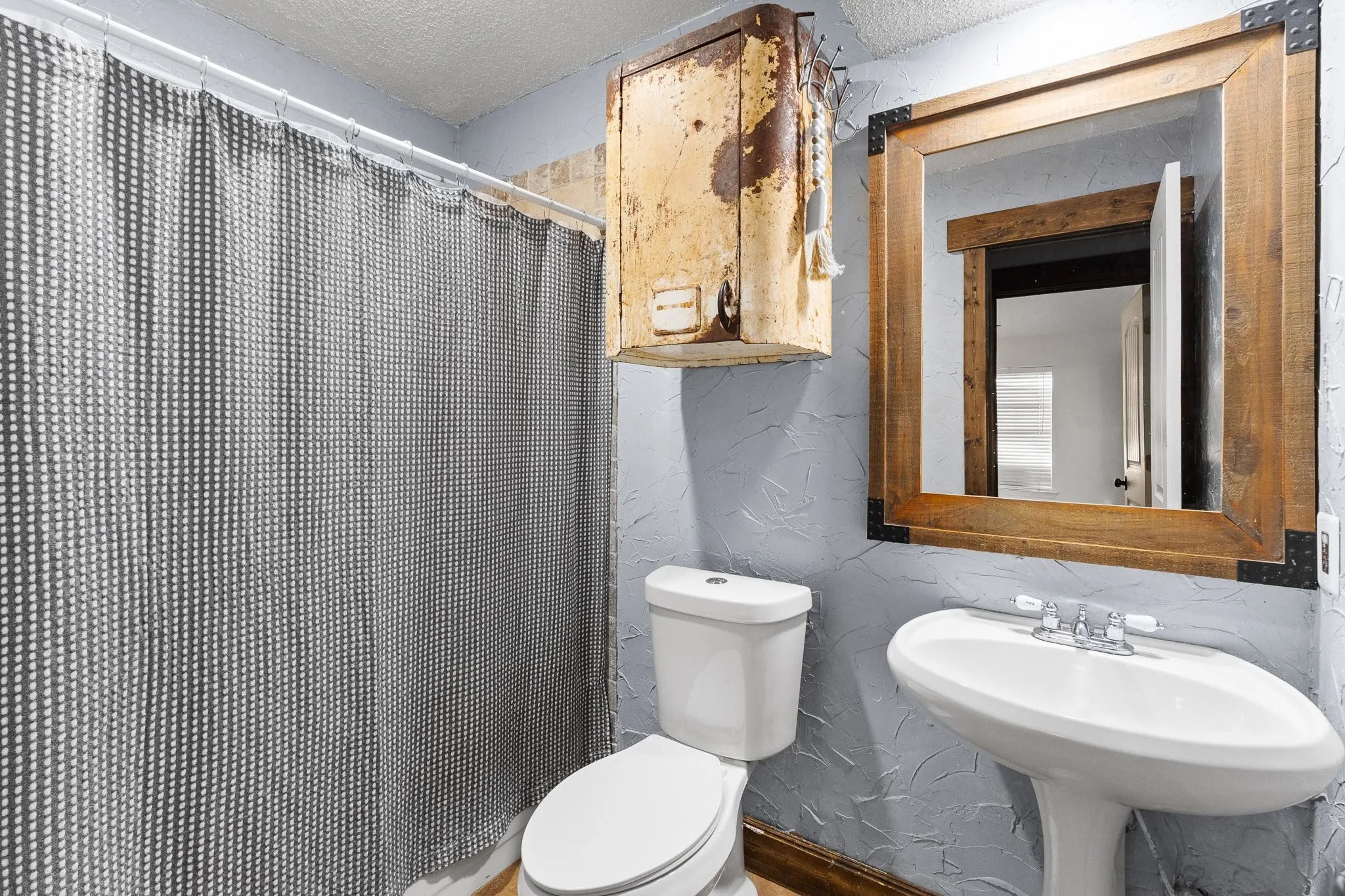Pedestal sink with chrome faucet, toilet, and a rustic wood-framed mirror