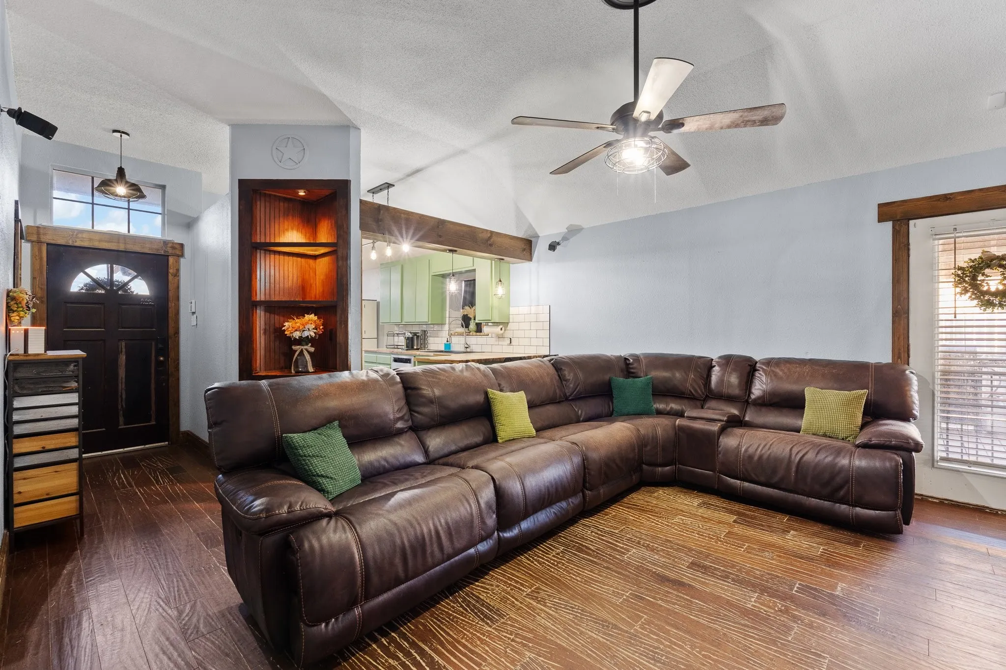 Vaulted ceiling with a ceiling fan, wood-finish flooring, built-in corner shelving with accent lighting, and a window with blinds