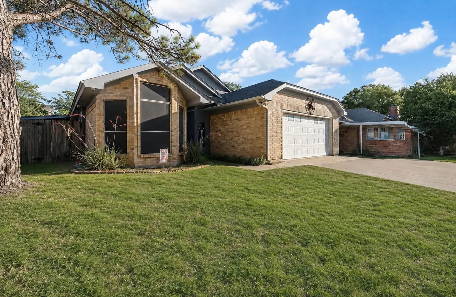 Brick exterior with a peaked roofline, attached garage, and mature tree