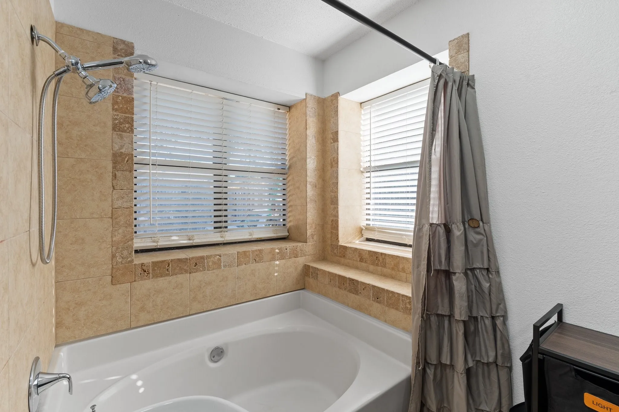 Built-in bathtub with tiled surround and multiple windows featuring horizontal blinds