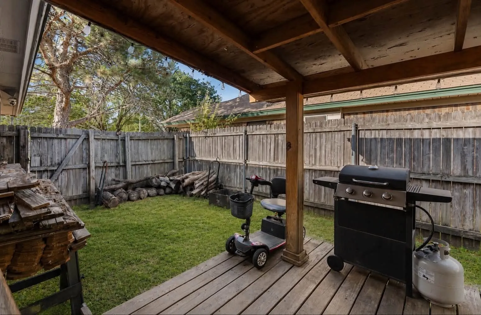 Covered wood deck with exposed beam ceiling, wood privacy fencing, and a grassy yard