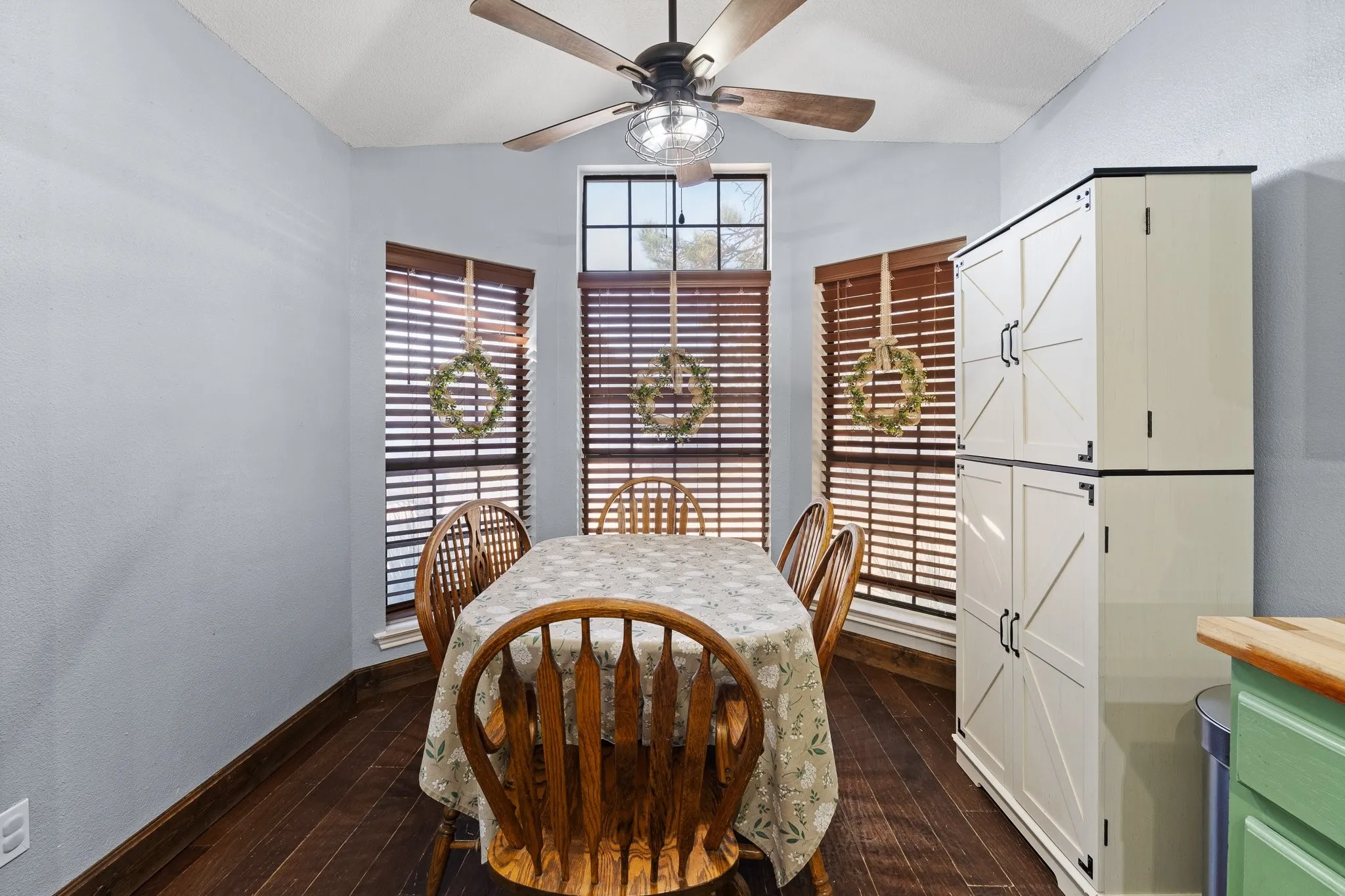 Vaulted ceiling with a ceiling fan, three windows with wood blinds, wood-finish flooring, and built-in storage cabinetry