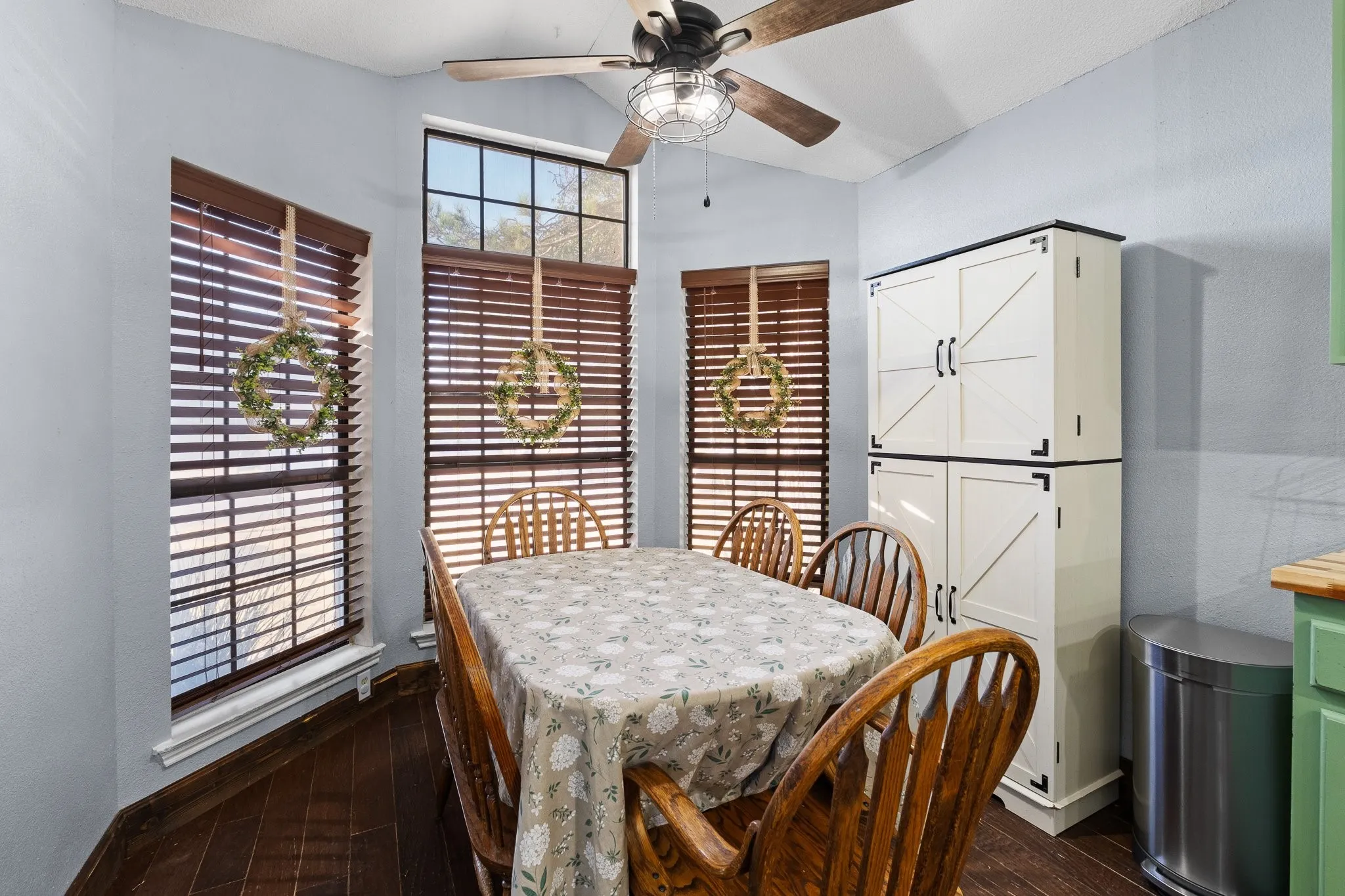 Wood-finish flooring, multiple windows with blinds, a ceiling fan, and built-in white cabinetry with black hardware