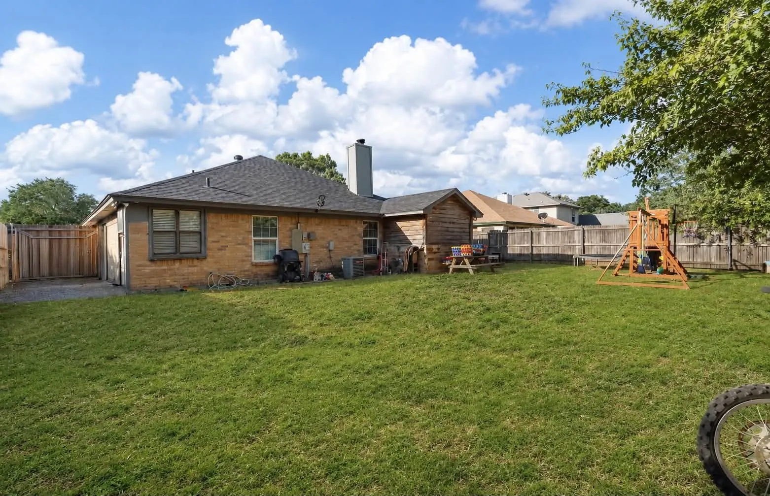 Expansive rear yard featuring a privacy fence, brick exterior, and a detached shed structure