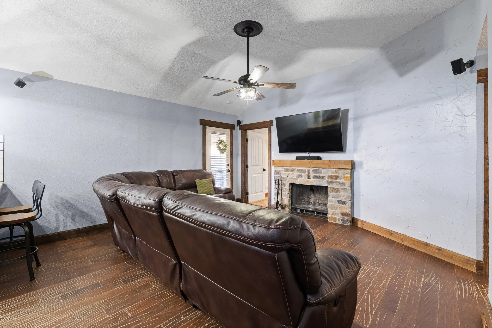Vaulted ceiling, wood-finish flooring, stone-front fireplace with wood mantle, ceiling fan, and recessed lighting