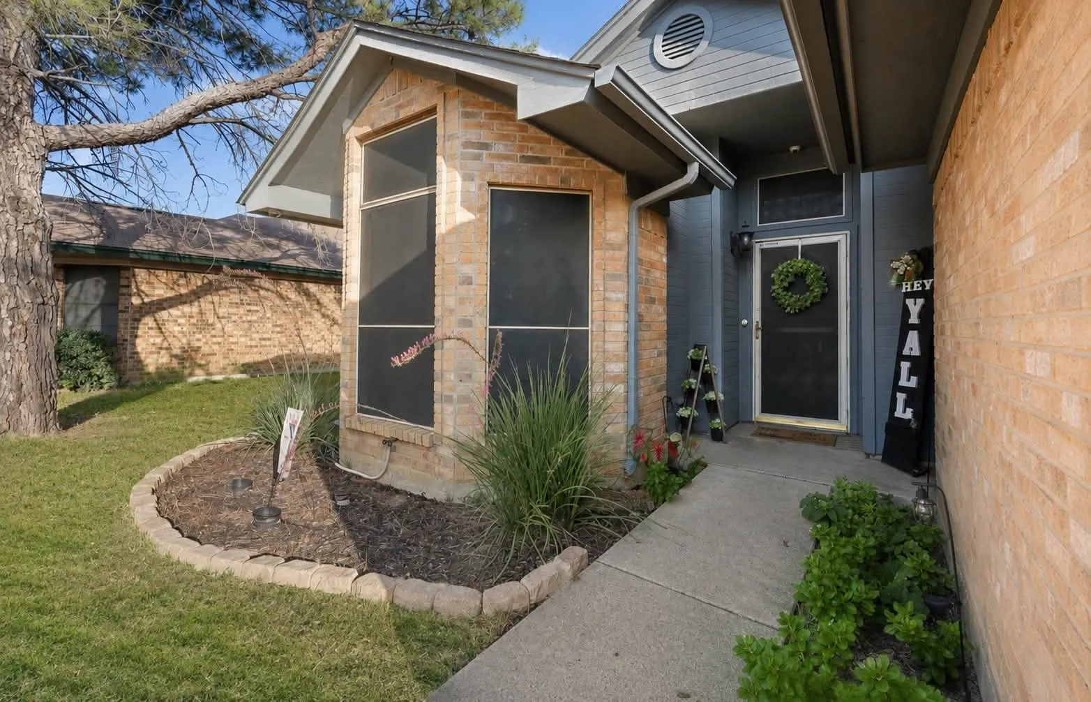 Brick and siding exterior featuring a covered entry, established landscaping, and a concrete pathway