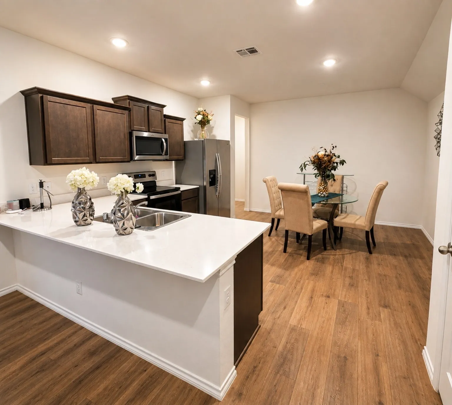 White countertops with an undermount sink, dark wood-finish cabinetry, stainless steel appliances, and wood-finish flooring