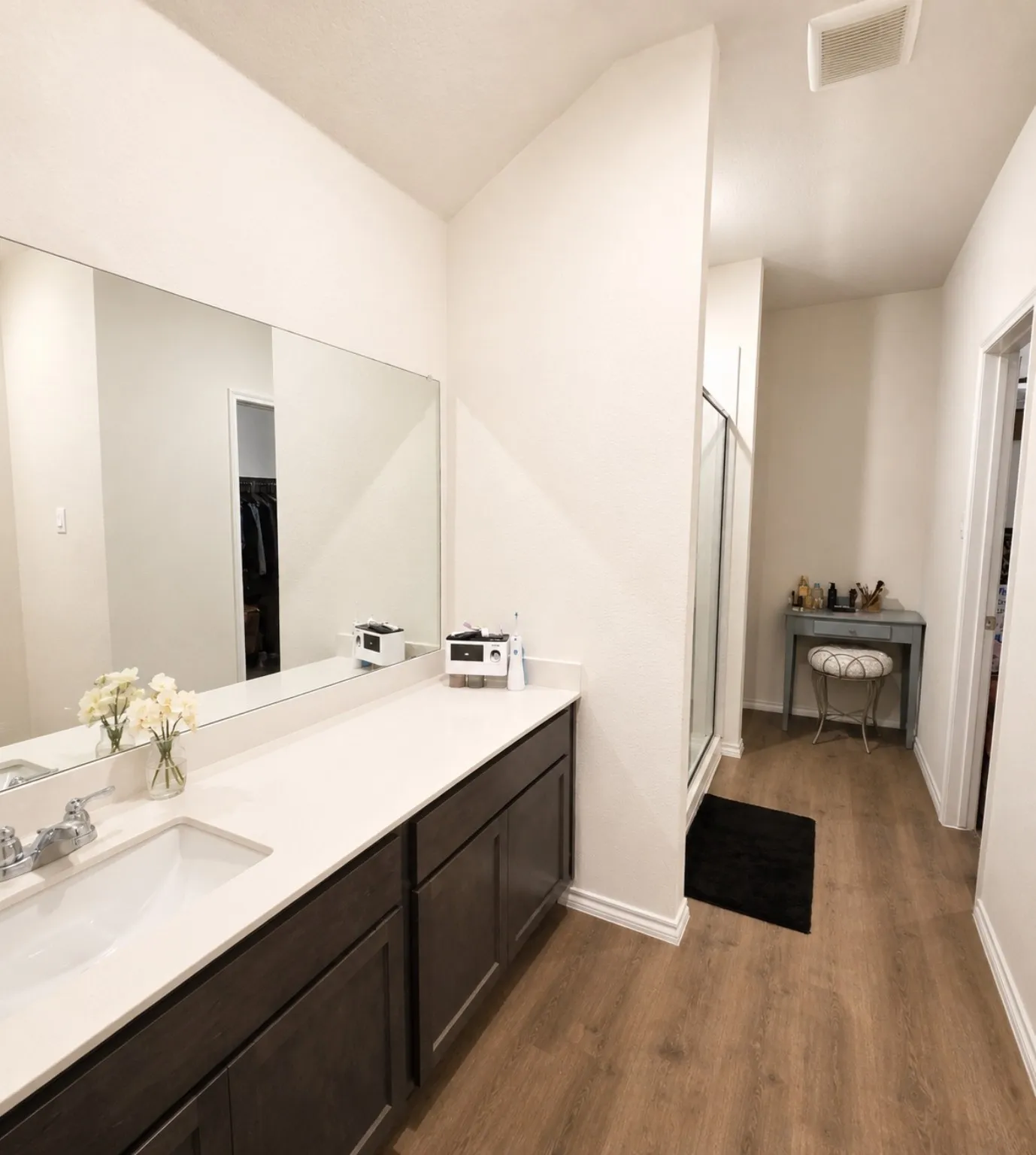 Double vanity with undermount sinks, expansive mirror, wood-finish flooring, and a glass-enclosed shower