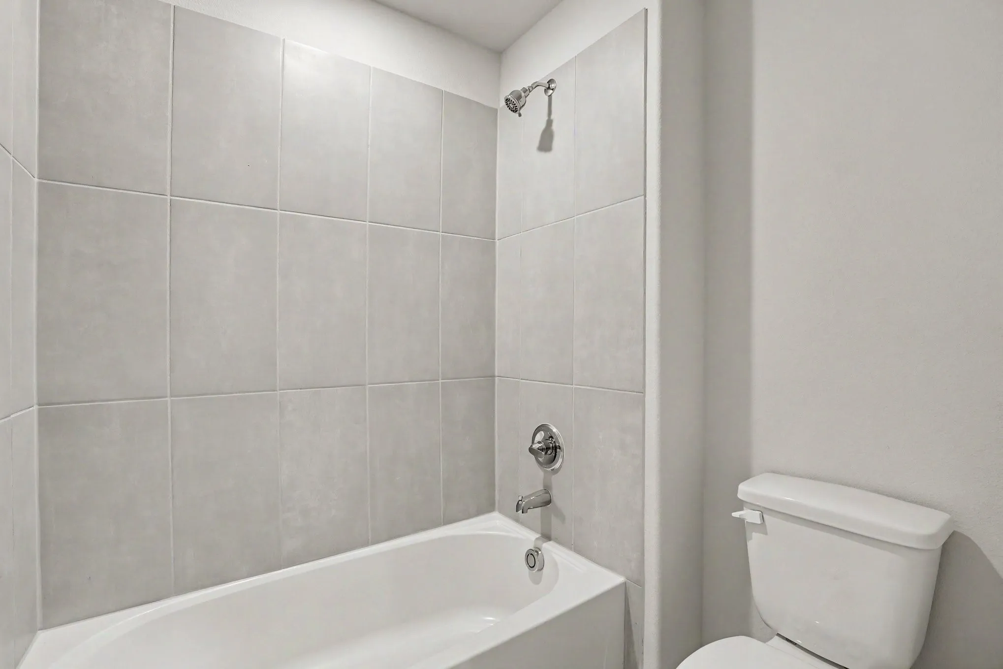 Bathtub and shower combination featuring large format grey wall tile and polished chrome fixtures