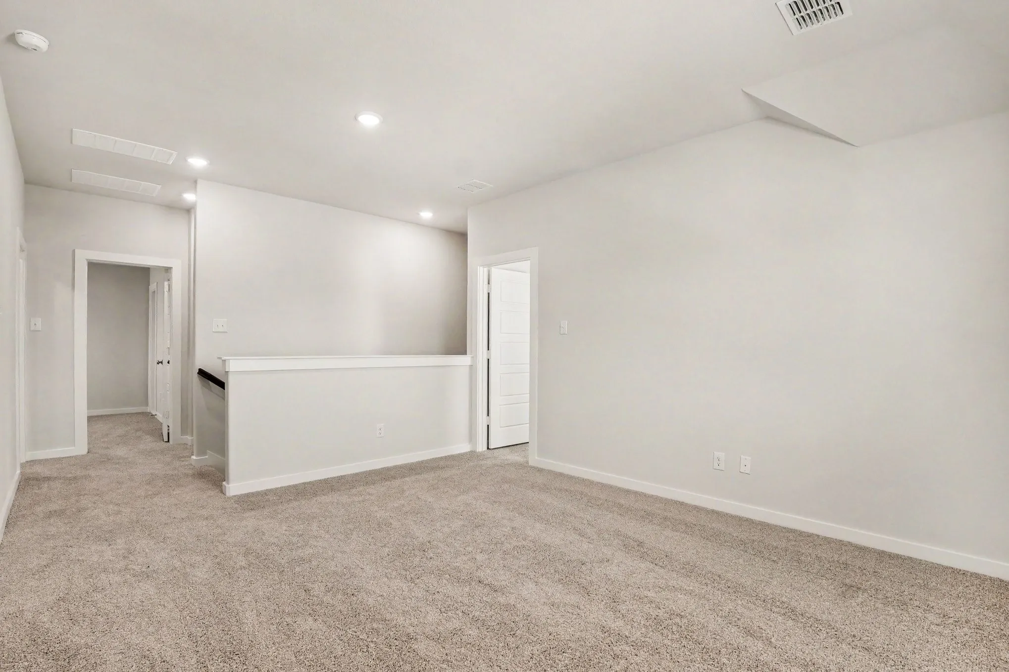 Carpeted room with recessed lighting, white walls, and a white half-wall railing
