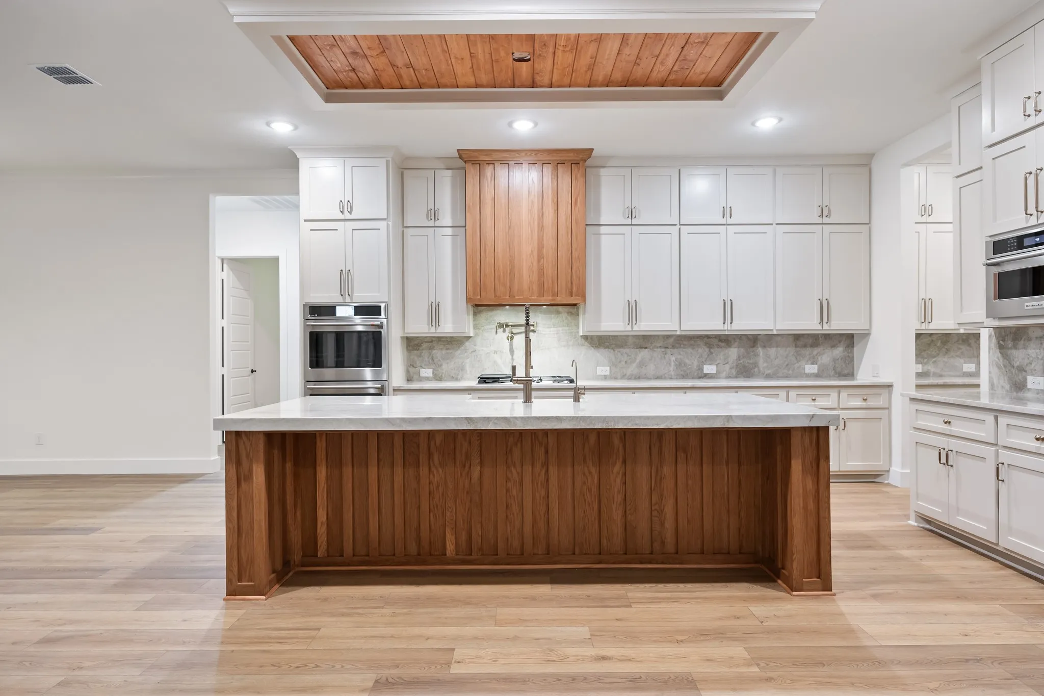 Kitchen with tasteful backsplash, light stone countertops, light wood-style floors, recessed lighting, and white cabinets!