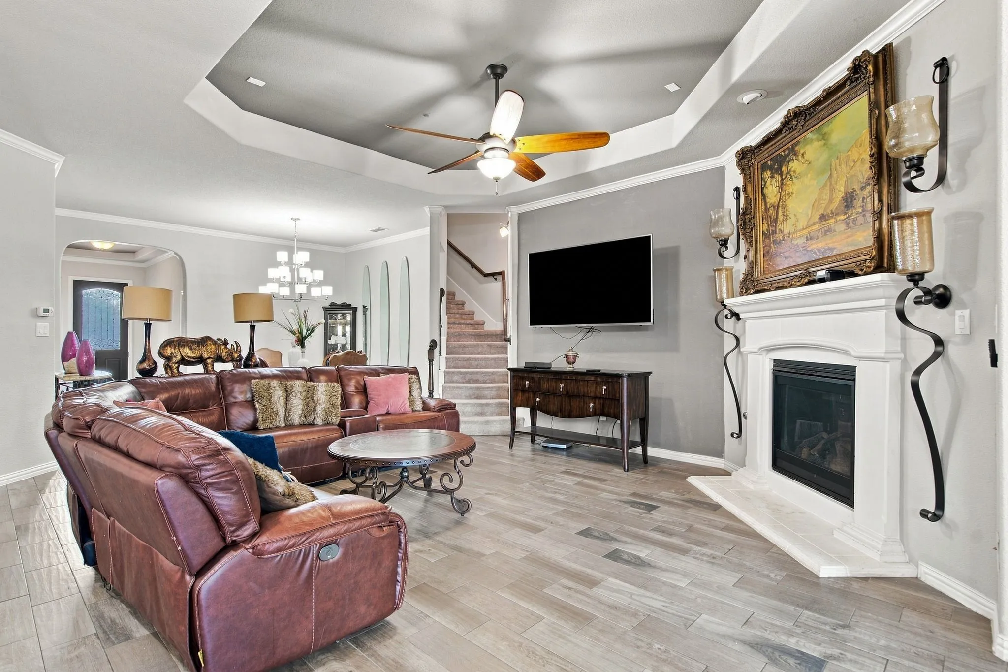 Tray ceiling with a ceiling fan, fireplace with a white mantel, wood-finish tile flooring, and recessed lighting