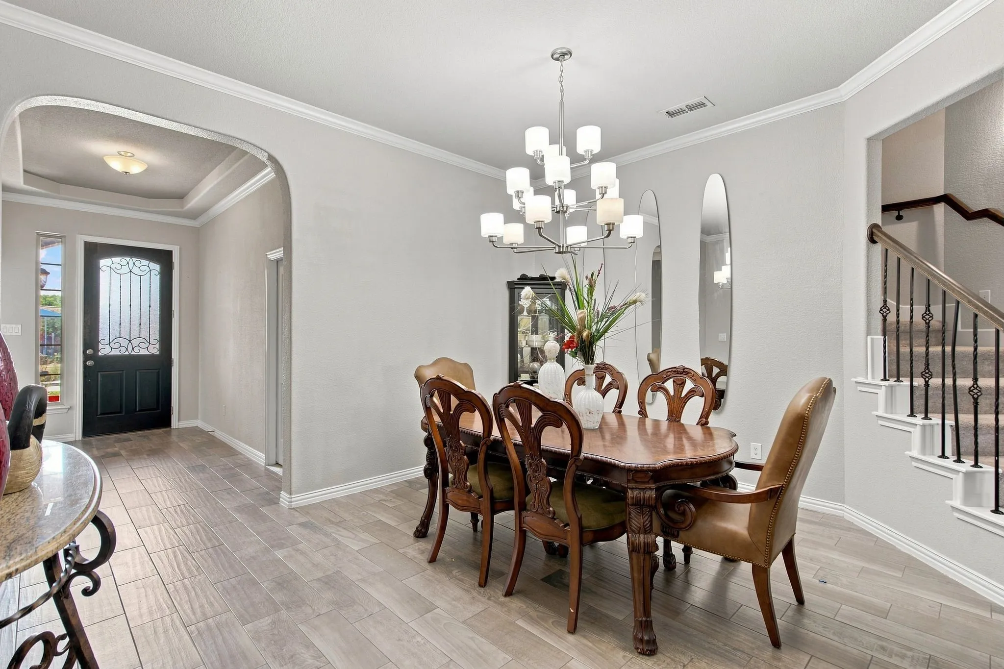 Arched entryway with a tray ceiling, wood-finish tile flooring, a decorative glass front door, and a staircase with wrought iron balusters