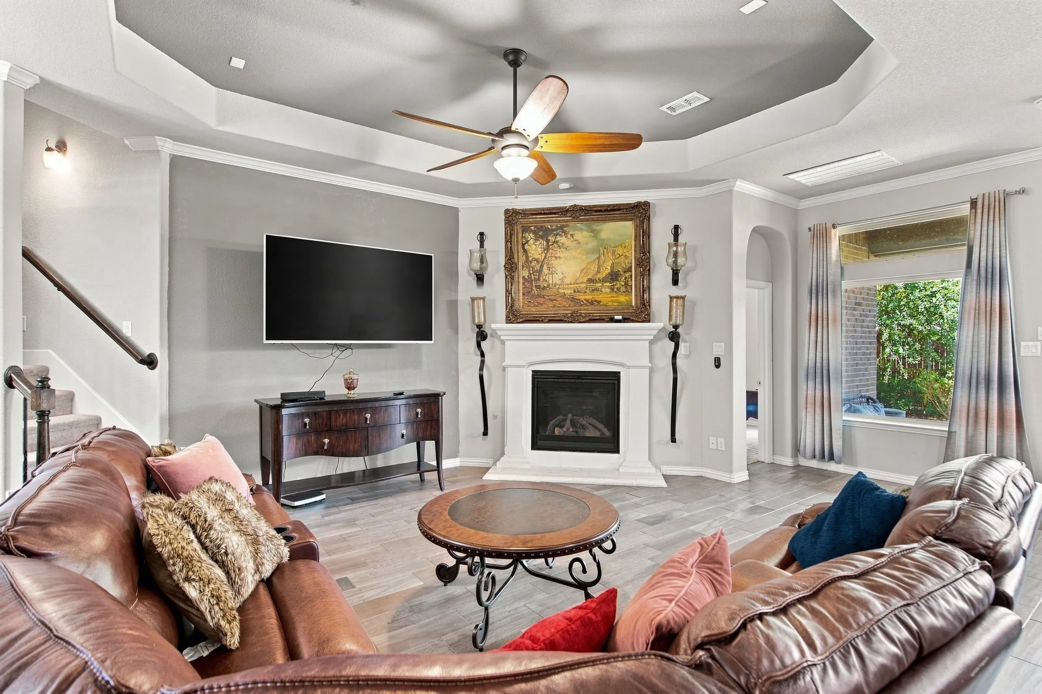 Living area with wood-finish tile flooring, a fireplace with a white mantel, and a tray ceiling with a ceiling fan