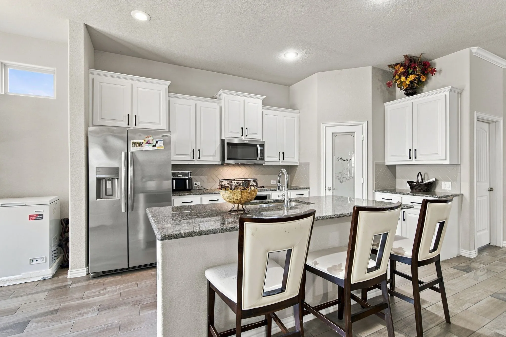 Kitchen featuring white cabinetry, stainless steel appliances, a granite-top island, a tile backsplash, and wood-finish Tile.