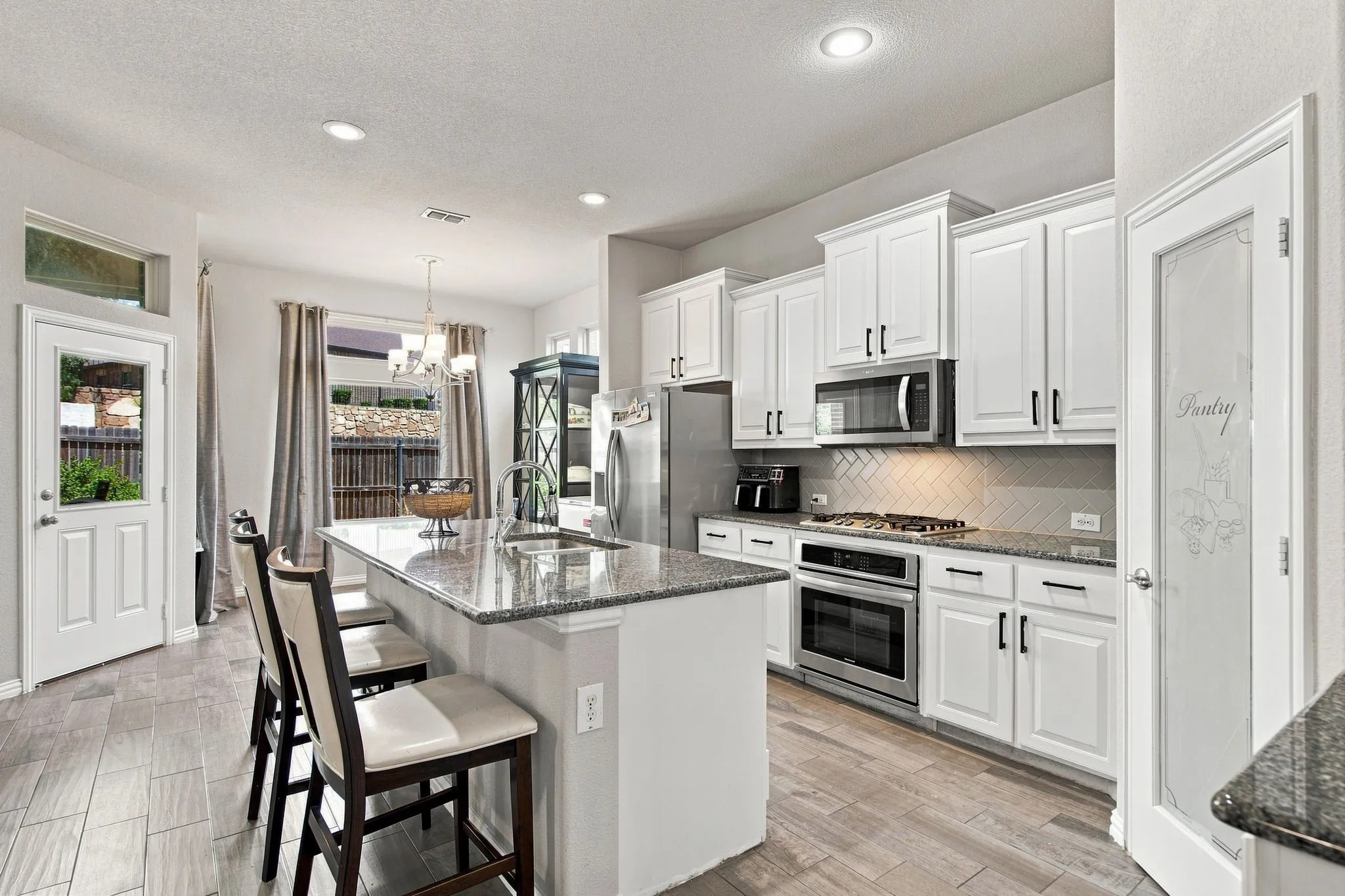 Gourmet kitchen featuring white cabinetry, stainless steel appliances, granite countertops, and wood-finish Tile.