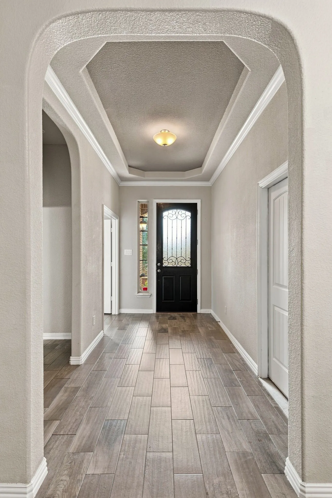 Arched entryway leading to an octagonal tray ceiling with crown molding, a decorative front door with transom window, and wood-look tile flooring