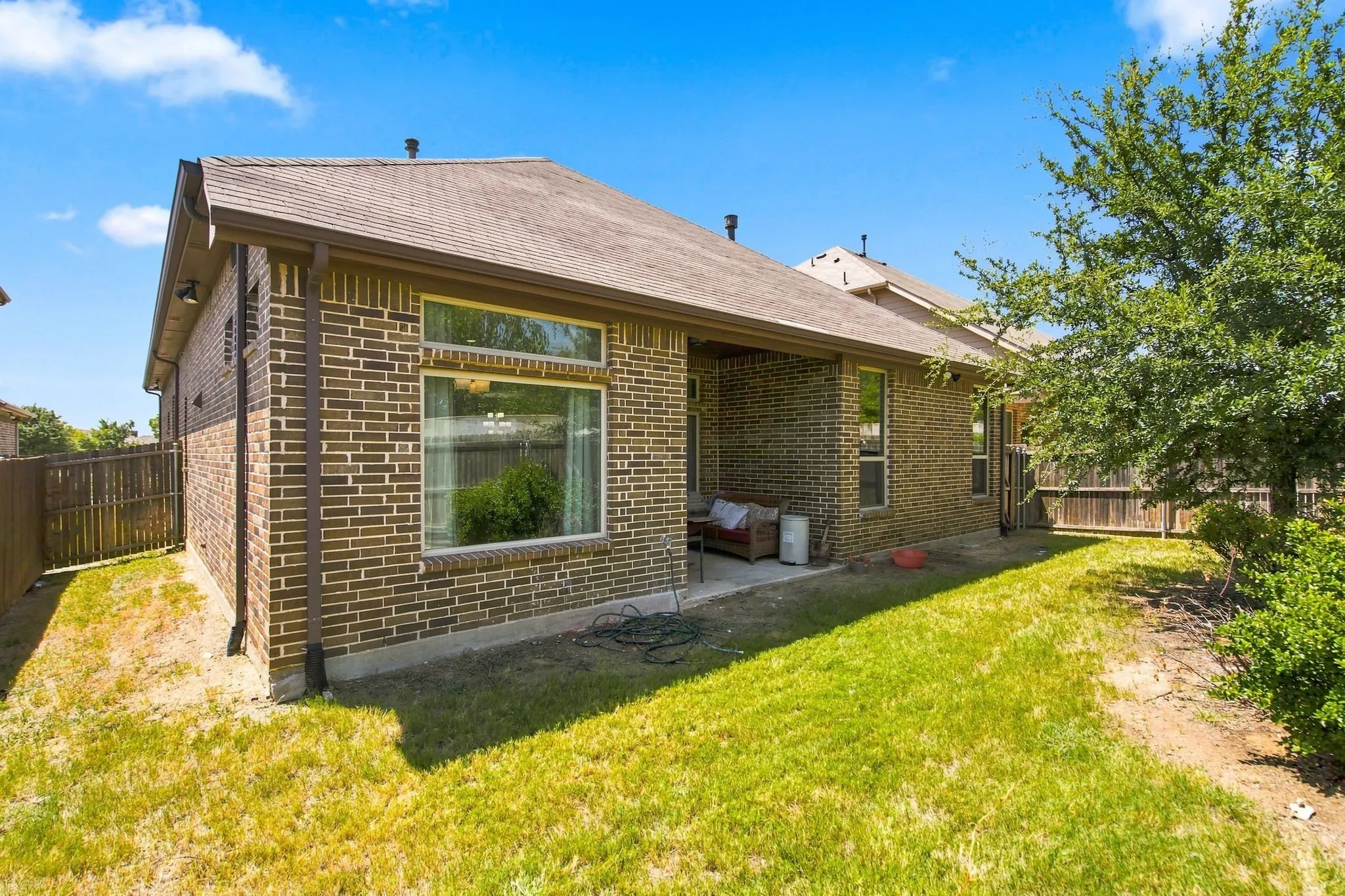 Brick exterior with a covered patio, fenced yard, and visible windows