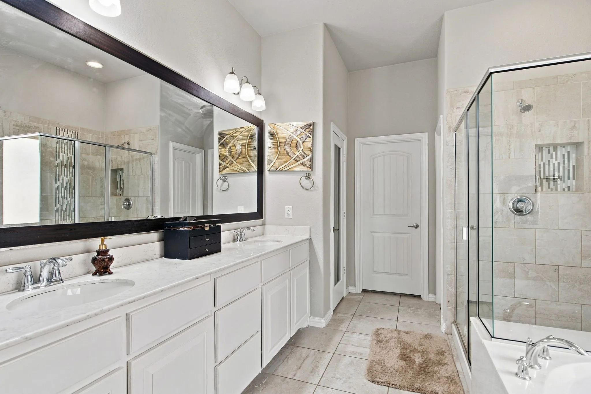 Dual vanity with white cabinetry and integrated sinks, extensive countertop space, large framed mirror, and a glass-enclosed shower with tiled surround