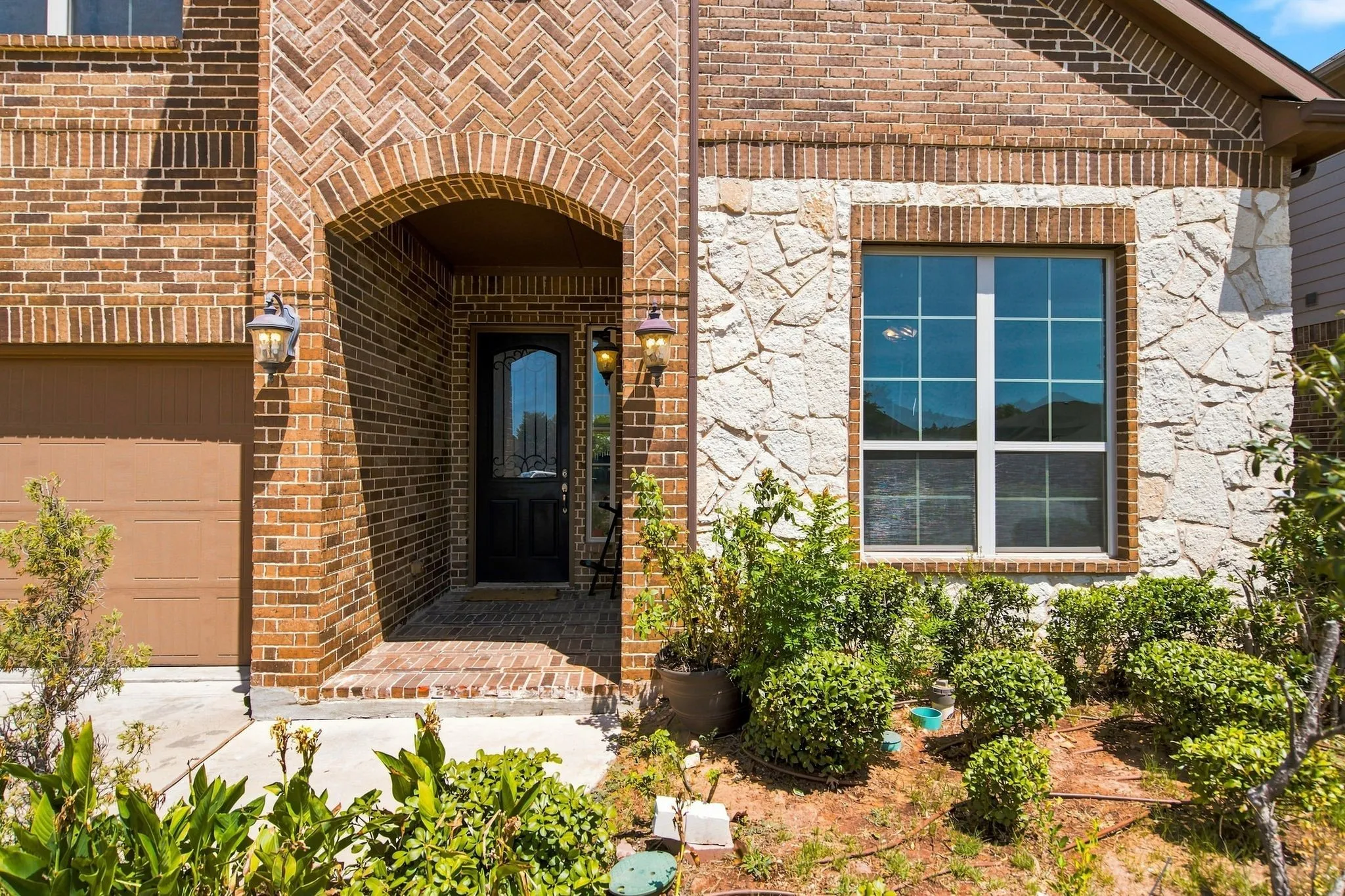 Brick exterior with herringbone accents, arched entryway, stone veneer detailing, and a garage door