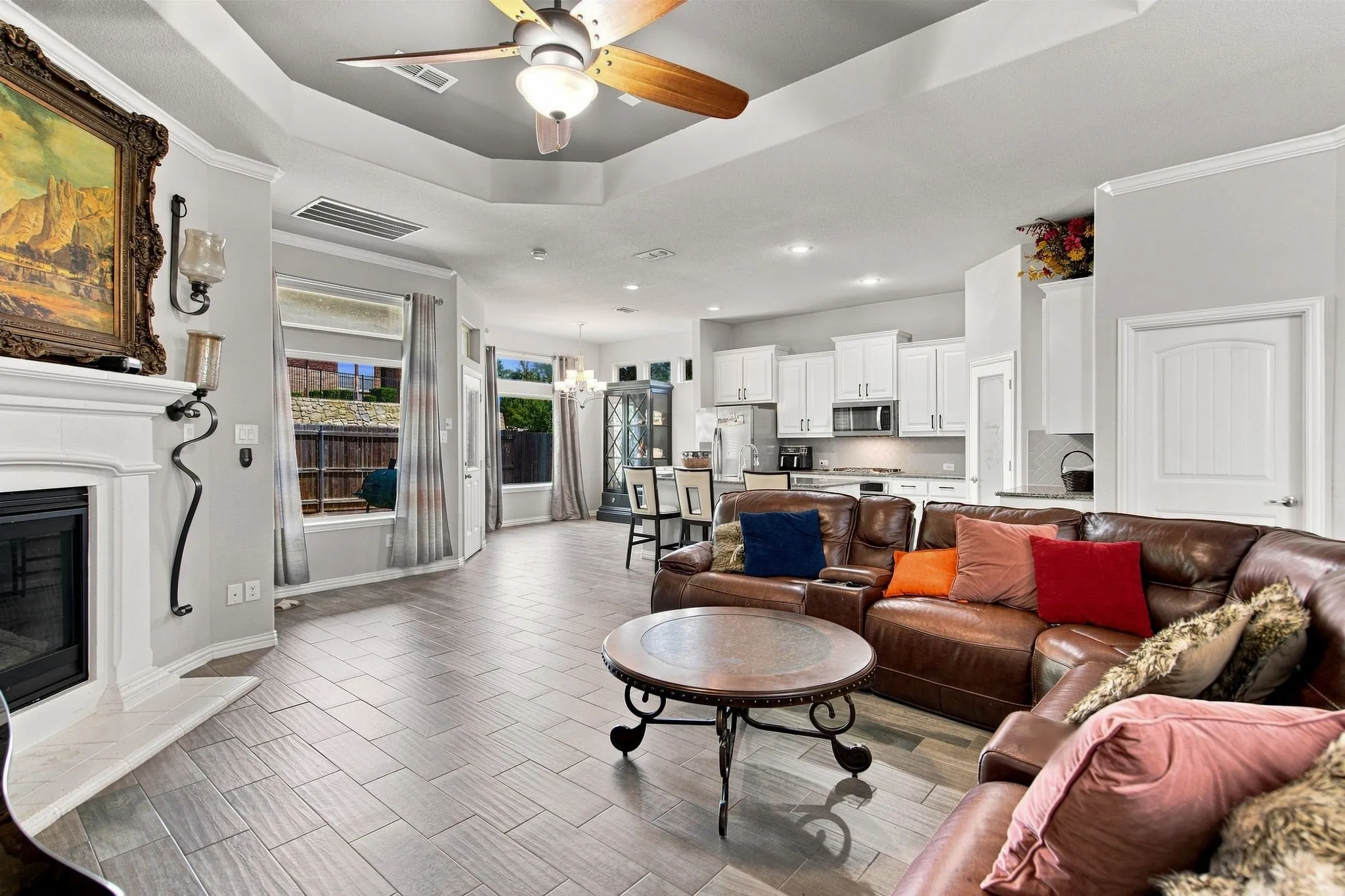 Open-concept living area featuring a fireplace with a mantel, wood-finish tile flooring, a tray ceiling with a fan, and recessed lighting