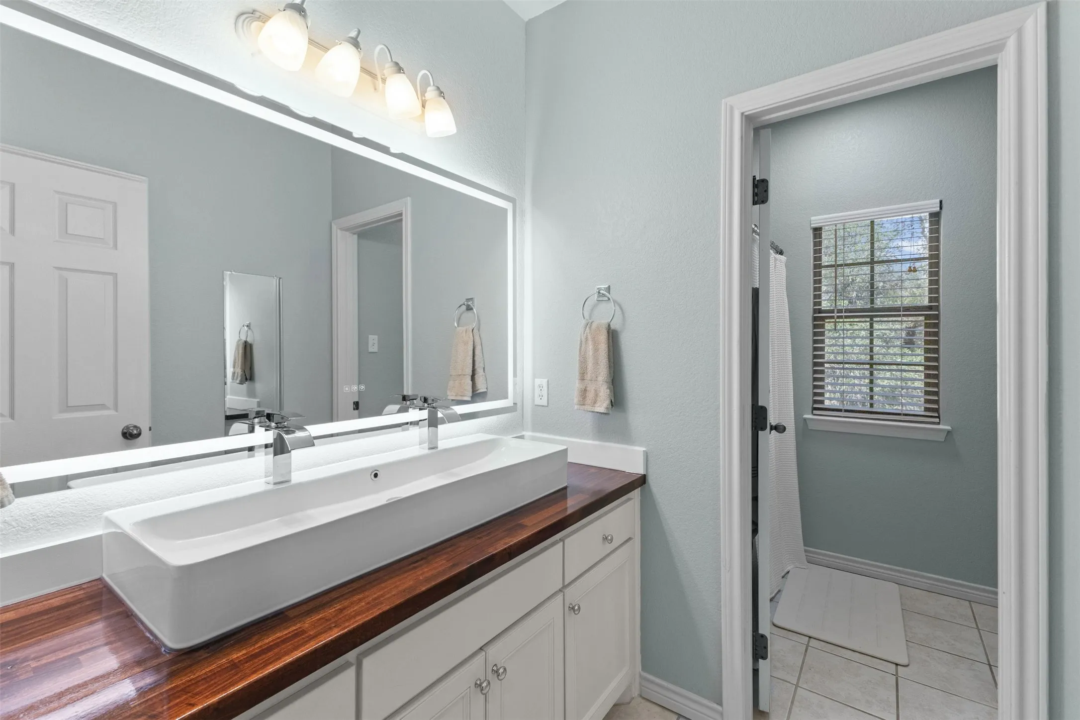 Vanity with a wood-finish countertop, dual vessel sinks, and an illuminated mirror