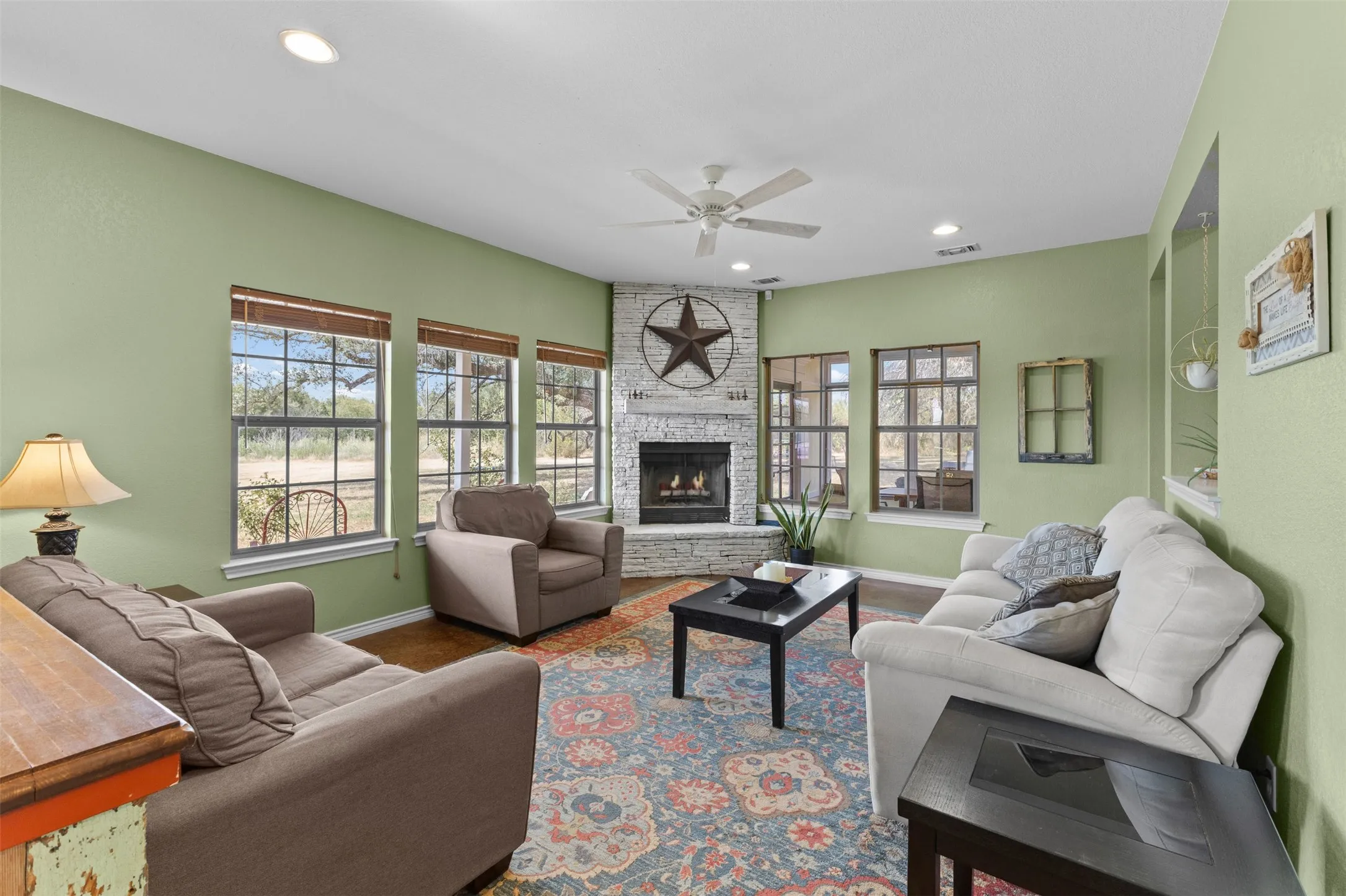 Corner fireplace with stone surround, recessed lighting, ceiling fan, multiple windows with grid panes, and built-in wall niches