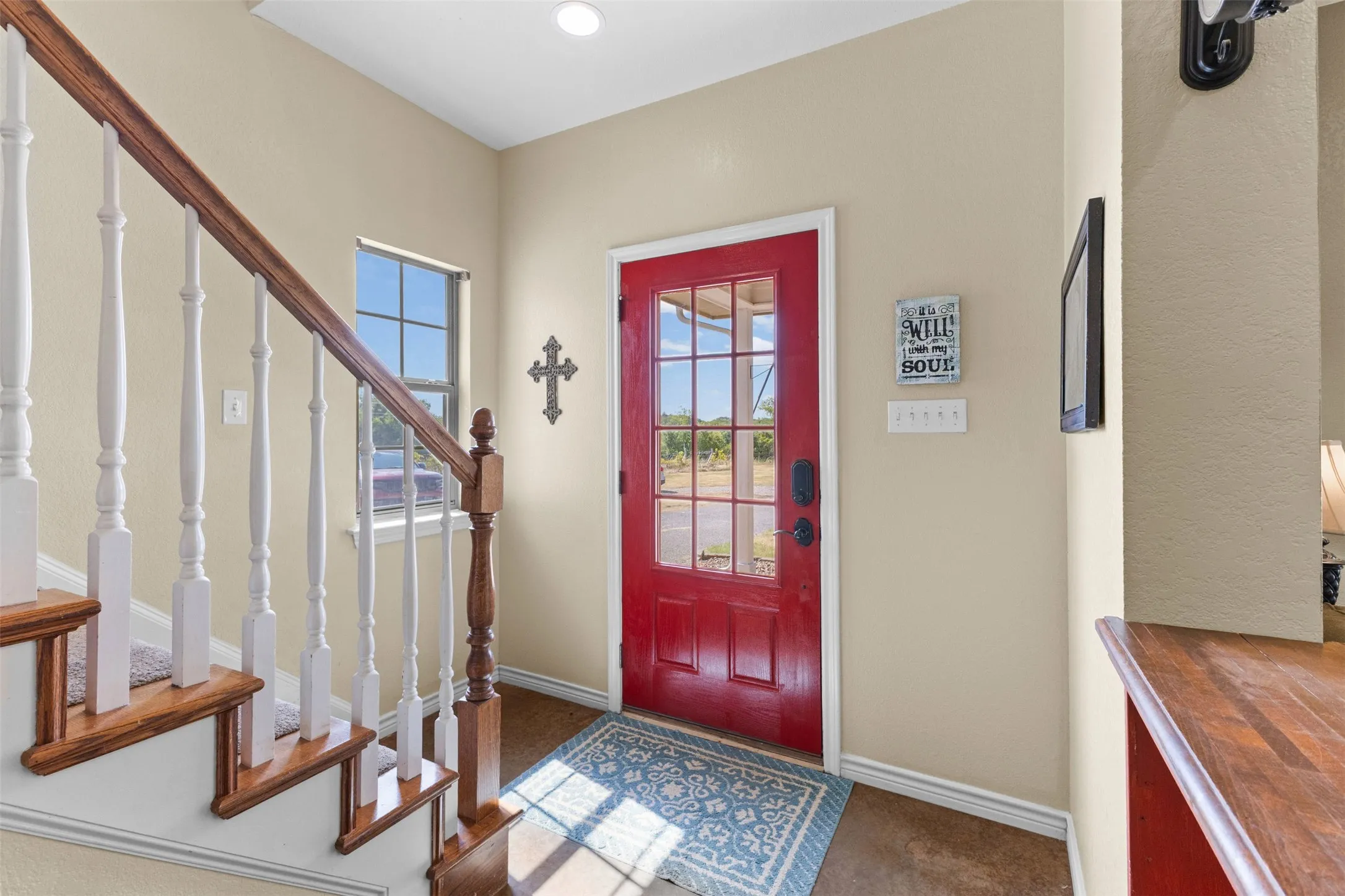 Warm red entry door with glass panels, wood-finish flooring, and a staircase featuring wood treads and white risers