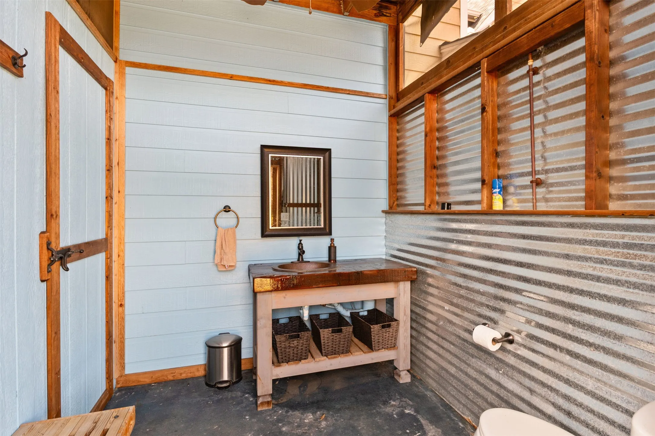 Open-air bathroom featuring a wood-finish vanity with an integrated sink, corrugated metal wall accents, and light blue wall paneling
