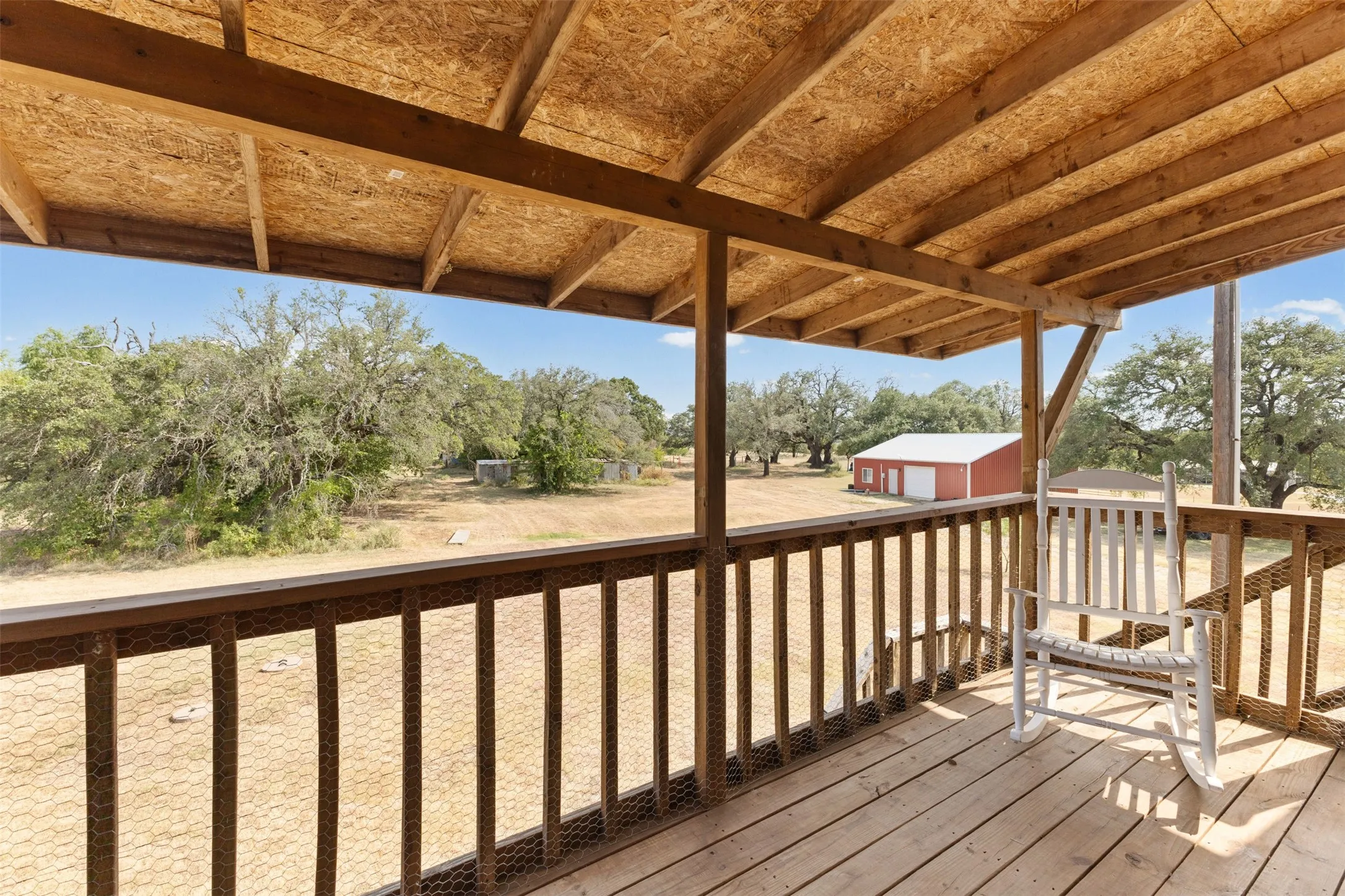 Covered wood-plank deck with wood railing, featuring an exposed wood-beam ceiling structure