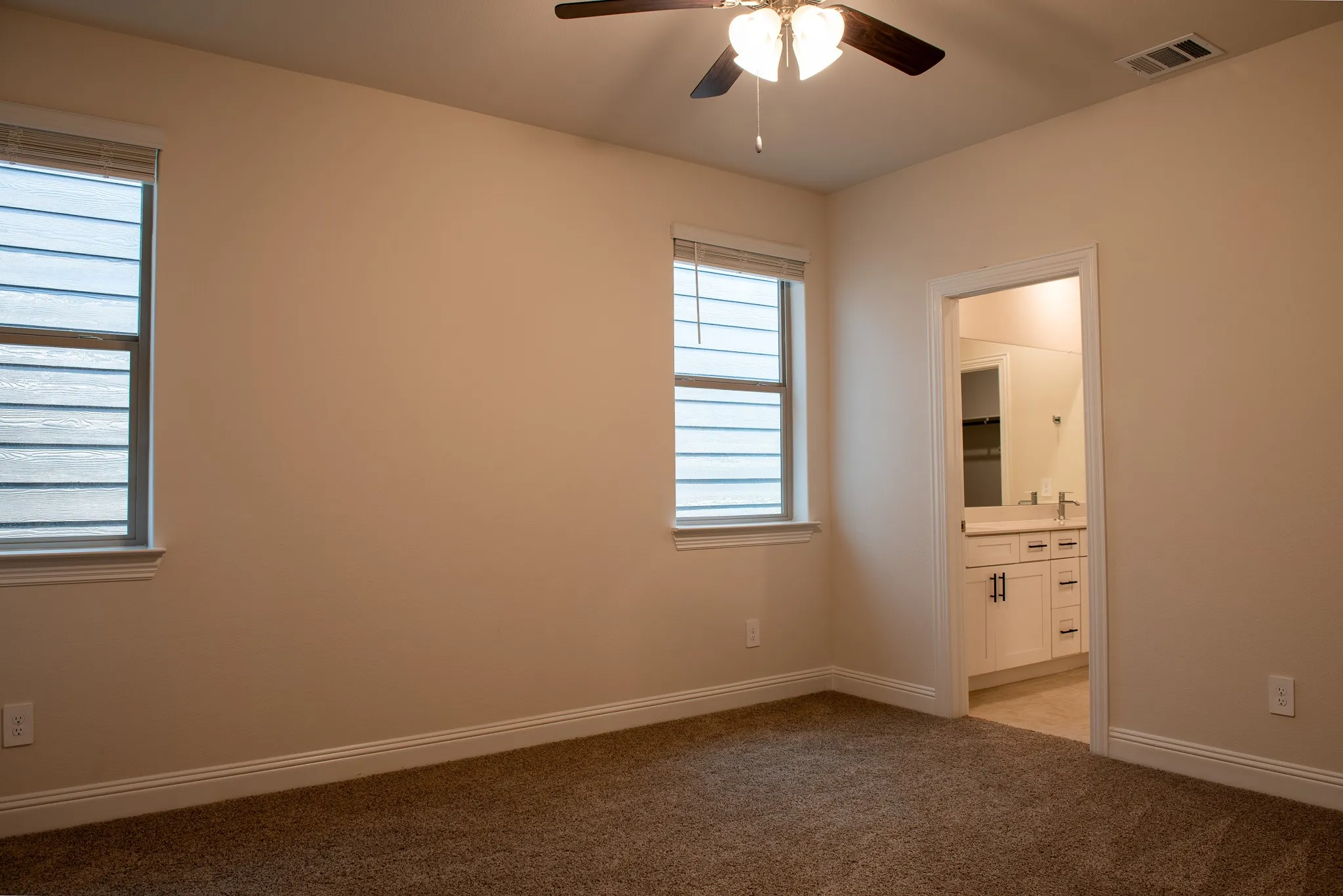 Spacious primary bedroom with neutral Pebble Path carpet, ceiling fan, and ensuite bath with walk-in closet.