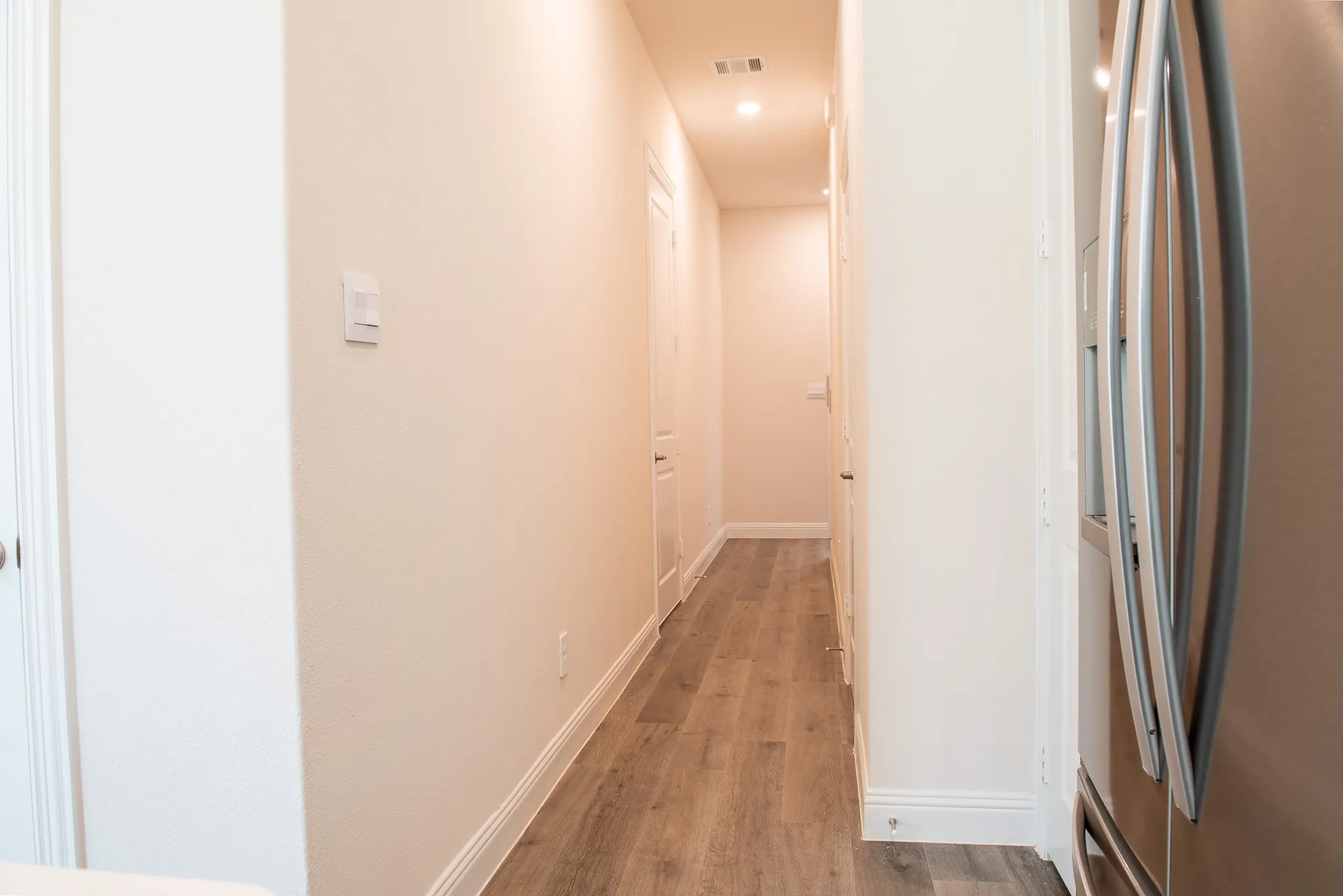 Hallway with durable wood-look luxury vinyl plank flooring, leading to garage entry and upstairs access.