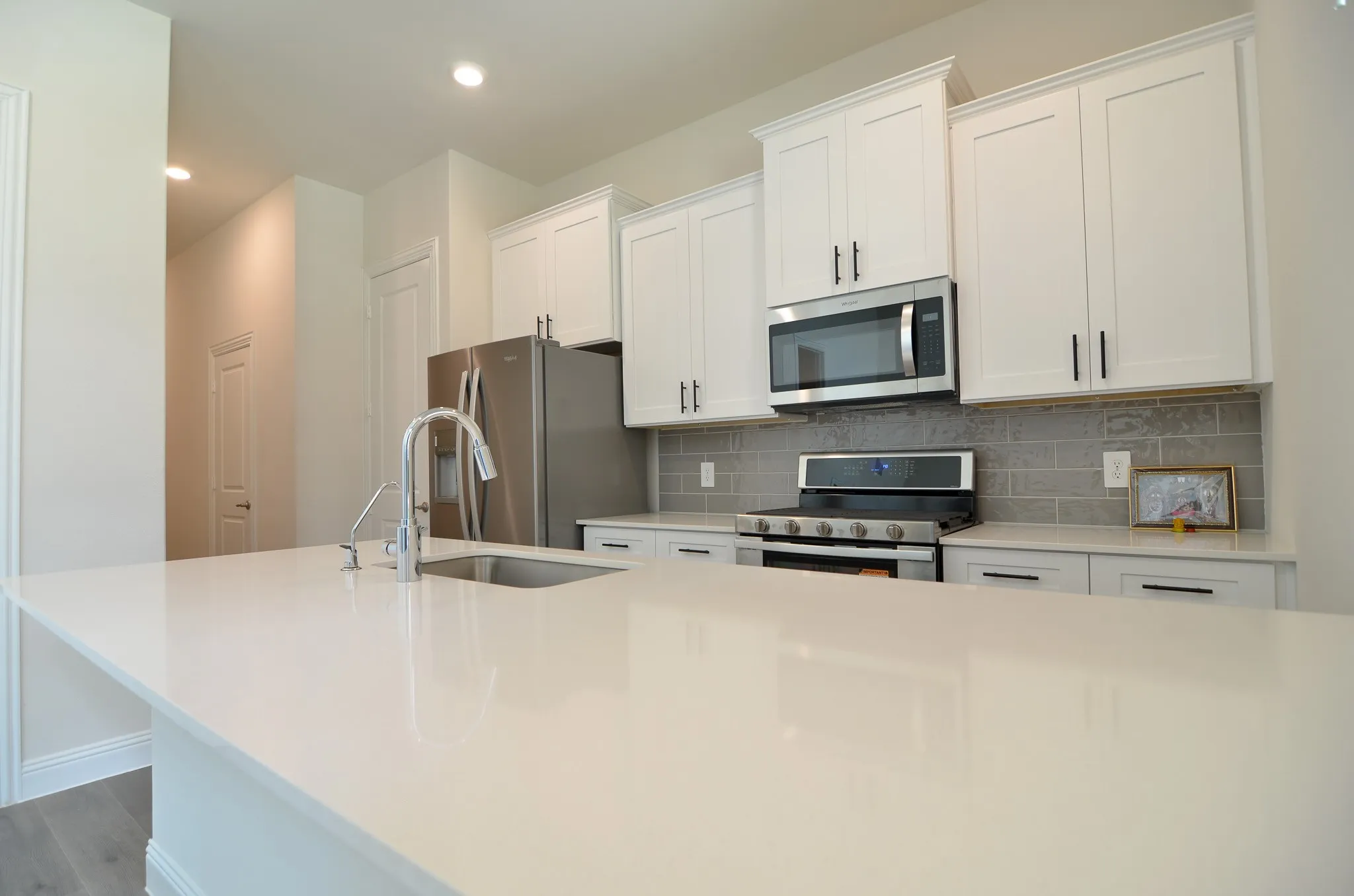 Modern kitchen with large quartz island, white shaker cabinets, stainless steel appliances, and gas range.