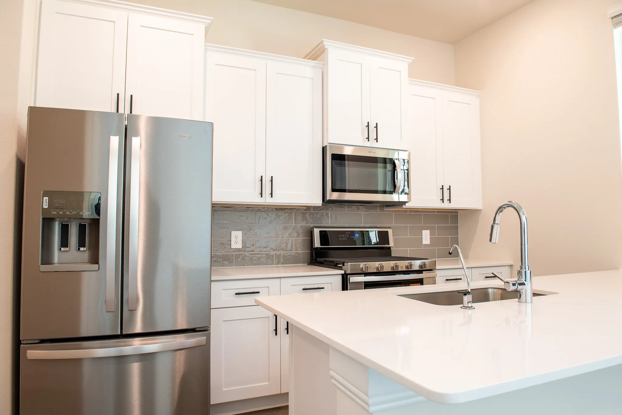 Kitchen features stainless steel refrigerator, microwave, gas range, quartz counters, and white soft-close cabinets.