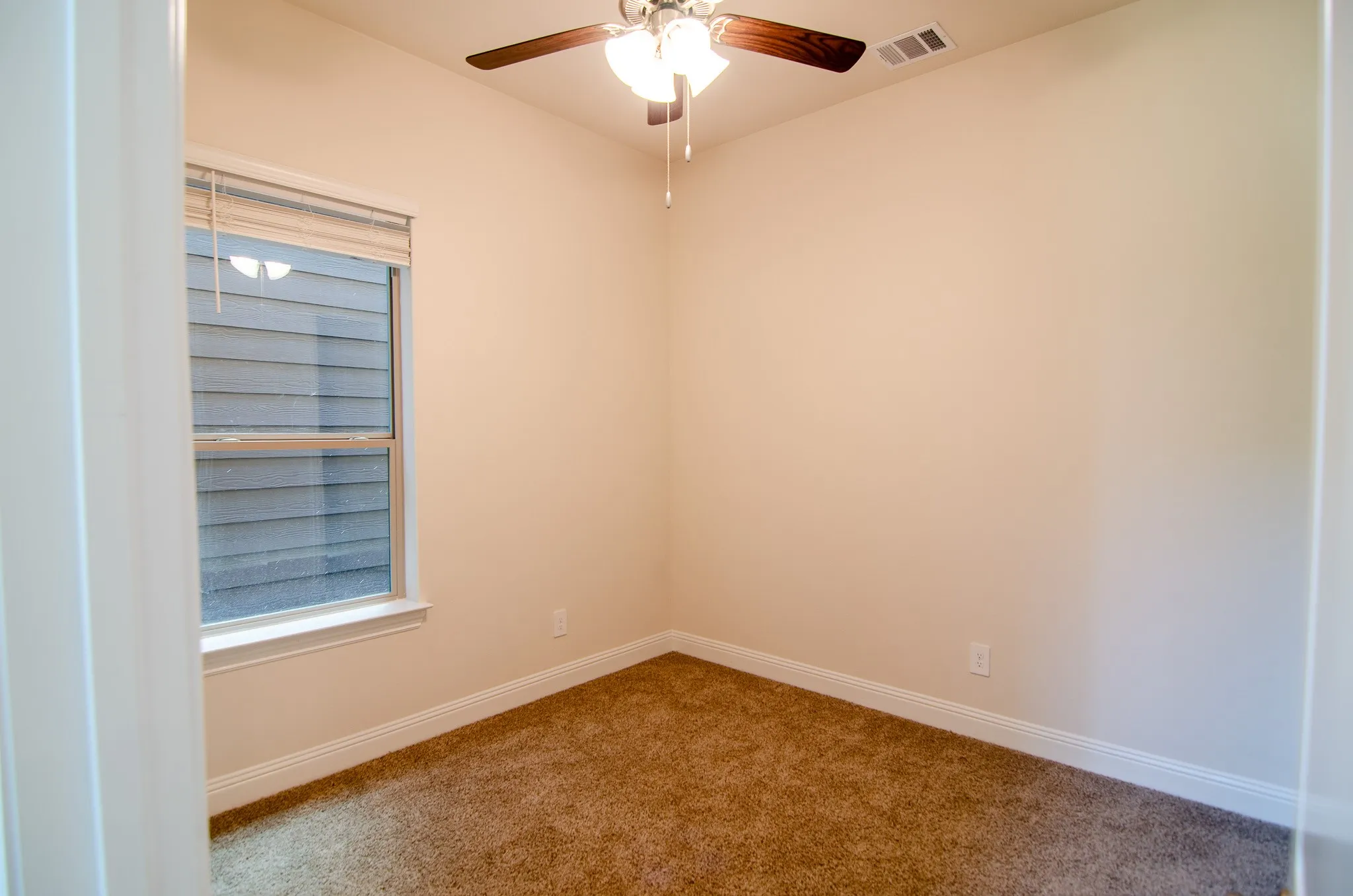 Spacious downstairs third bedroom featuring plush carpet flooring, ceiling fan with light, and a large window providing natural light—perfect for use as a guest room, home office, or flex space.
