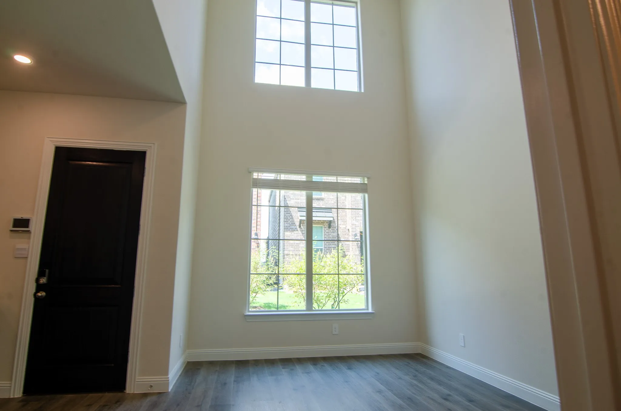 Bright downstairs living room with soaring two-story ceilings, large windows, and wood-look flooring.