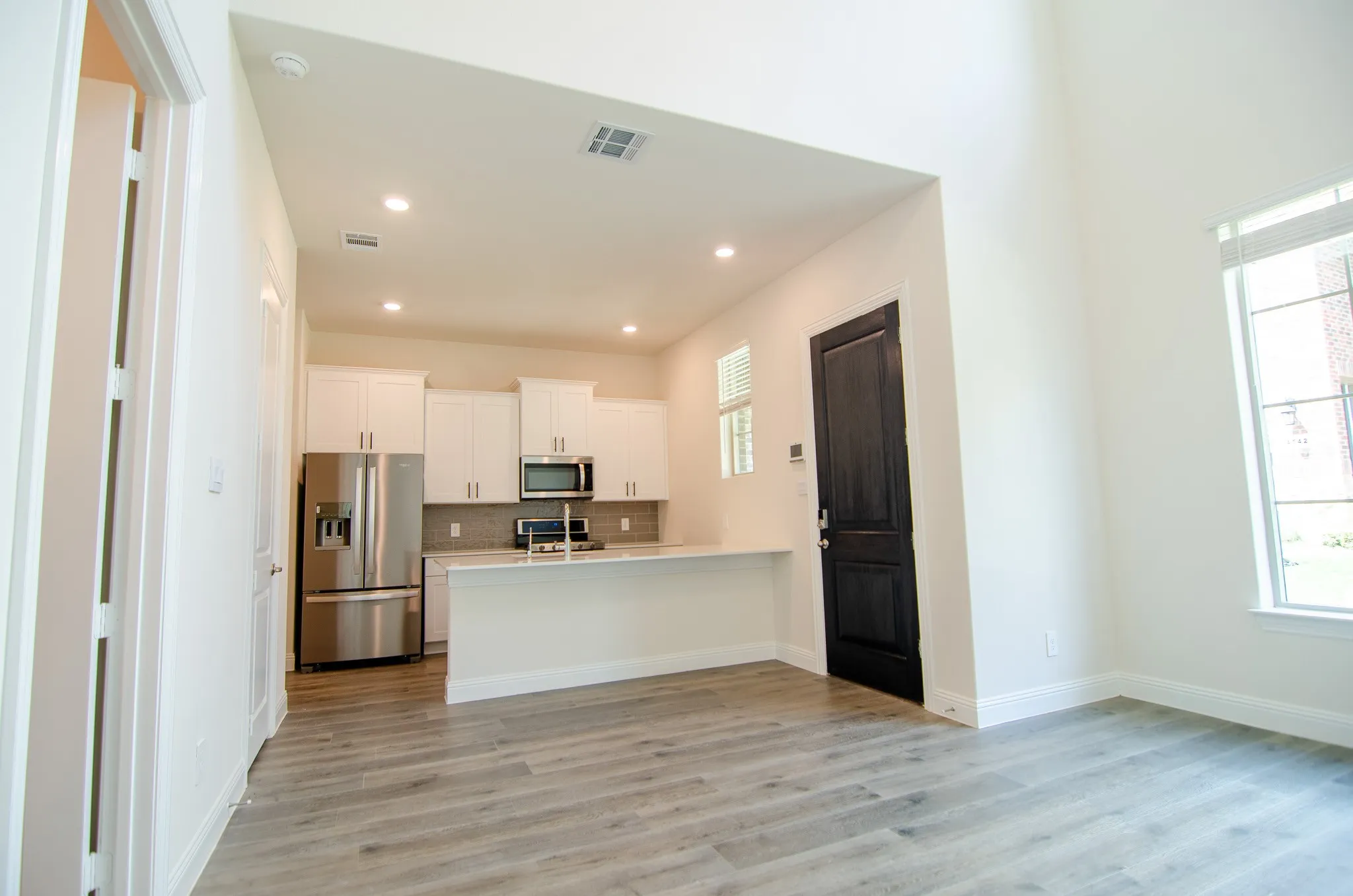 Spacious living area with soaring ceilings, wood-look flooring, and open flow into the modern kitchen.